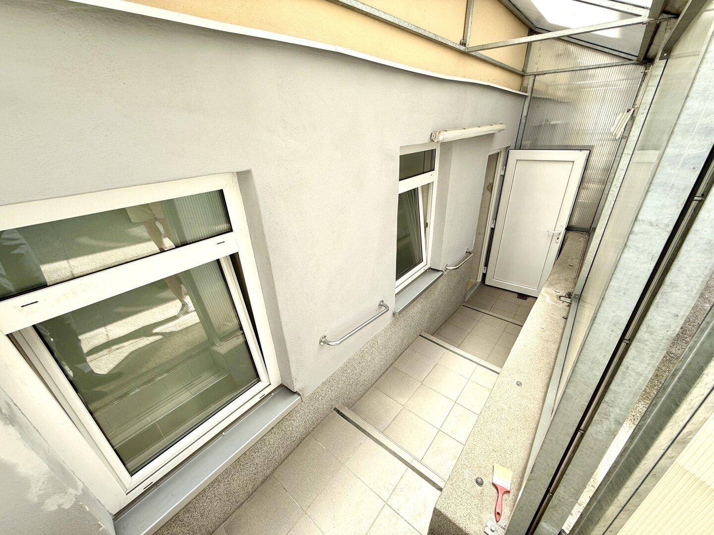 Überdachter Eingangsbereich mit Treppe und Fenstern, der zu den Räumlichkeiten führt.
