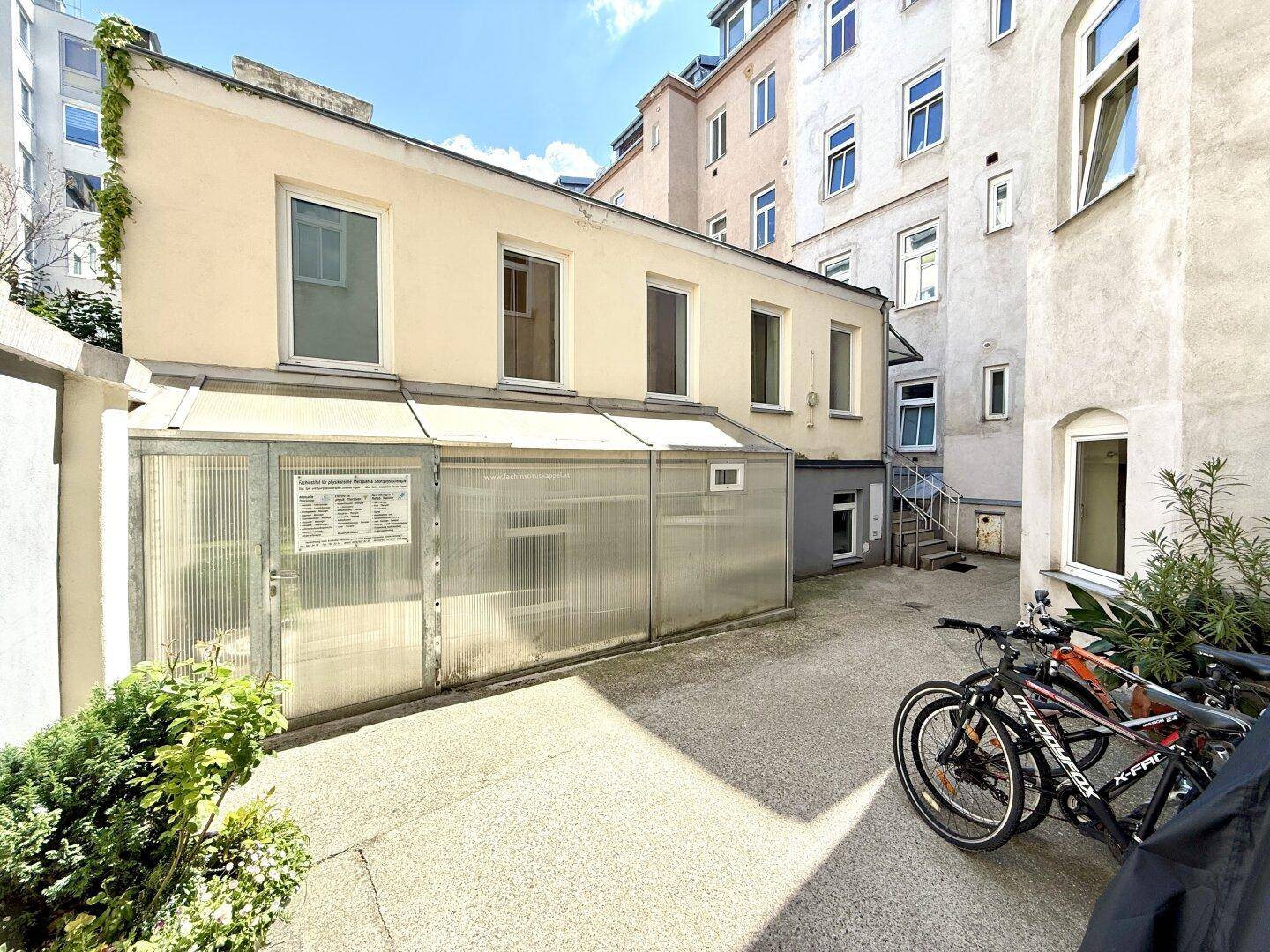Innenhof mit Fahrradabstellplatz und Zugang zu einem Nebengebäude, umgeben von Wohngebäuden.
