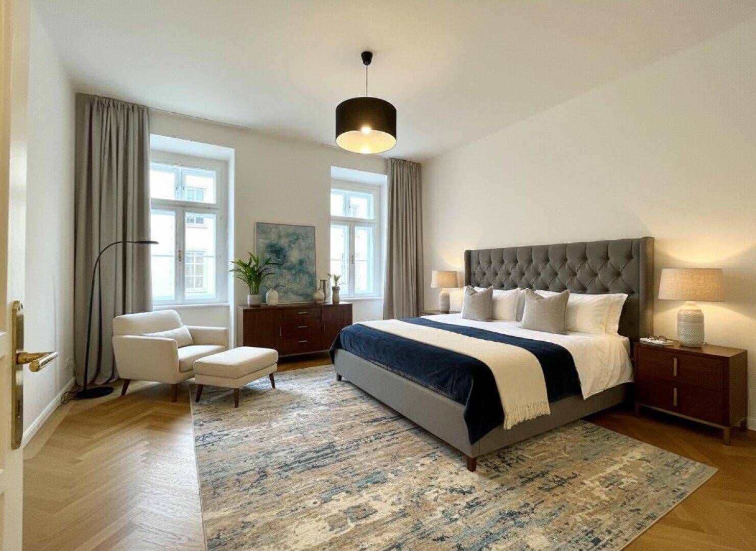 Helles Schlafzimmer mit großem Bett, bequemer Sitzecke und Fischgrätparkettboden.