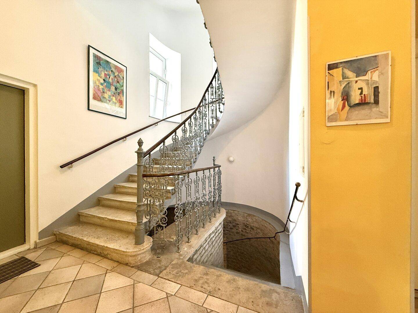 Historisches Treppenhaus mit schmiedeeisernem Geländer und gefliestem Boden in einem Altbau.
