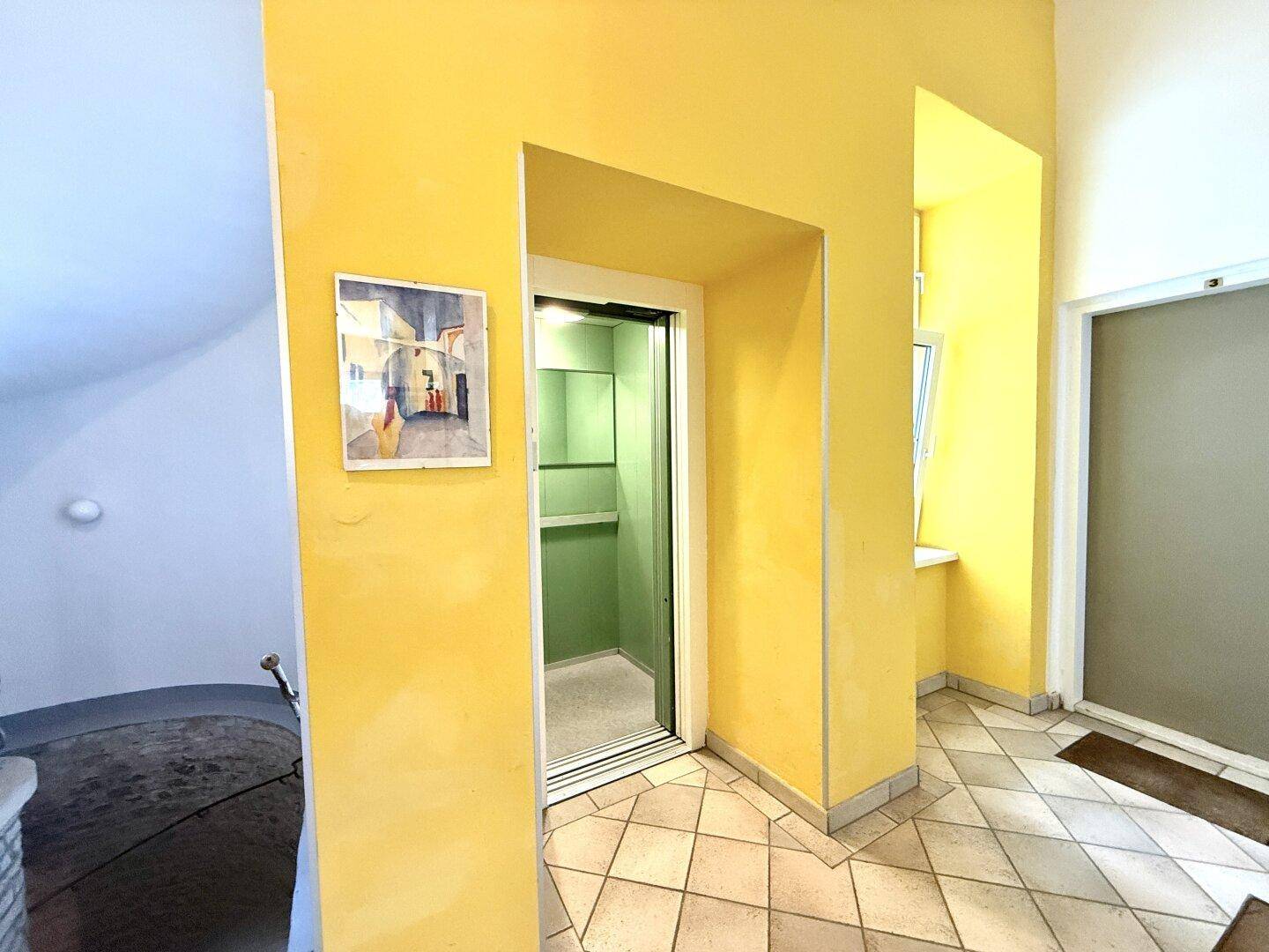 Heller Flur mit gelben Wänden und einem modernen Aufzug, der sich in einem Altbau befindet.