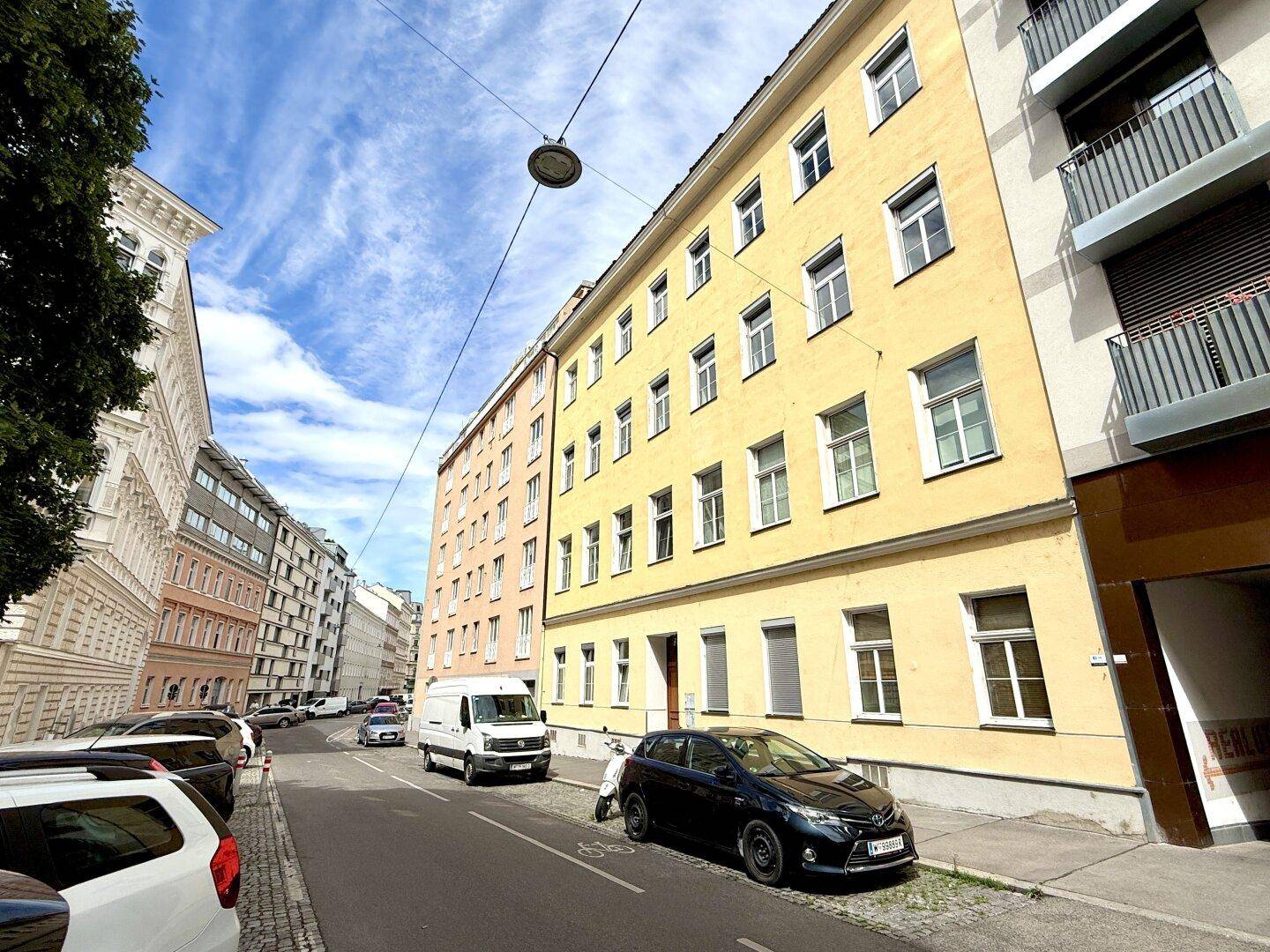 Ansicht eines gelben Mehrfamilienhauses an einer städtischen Straße mit parkenden Autos.