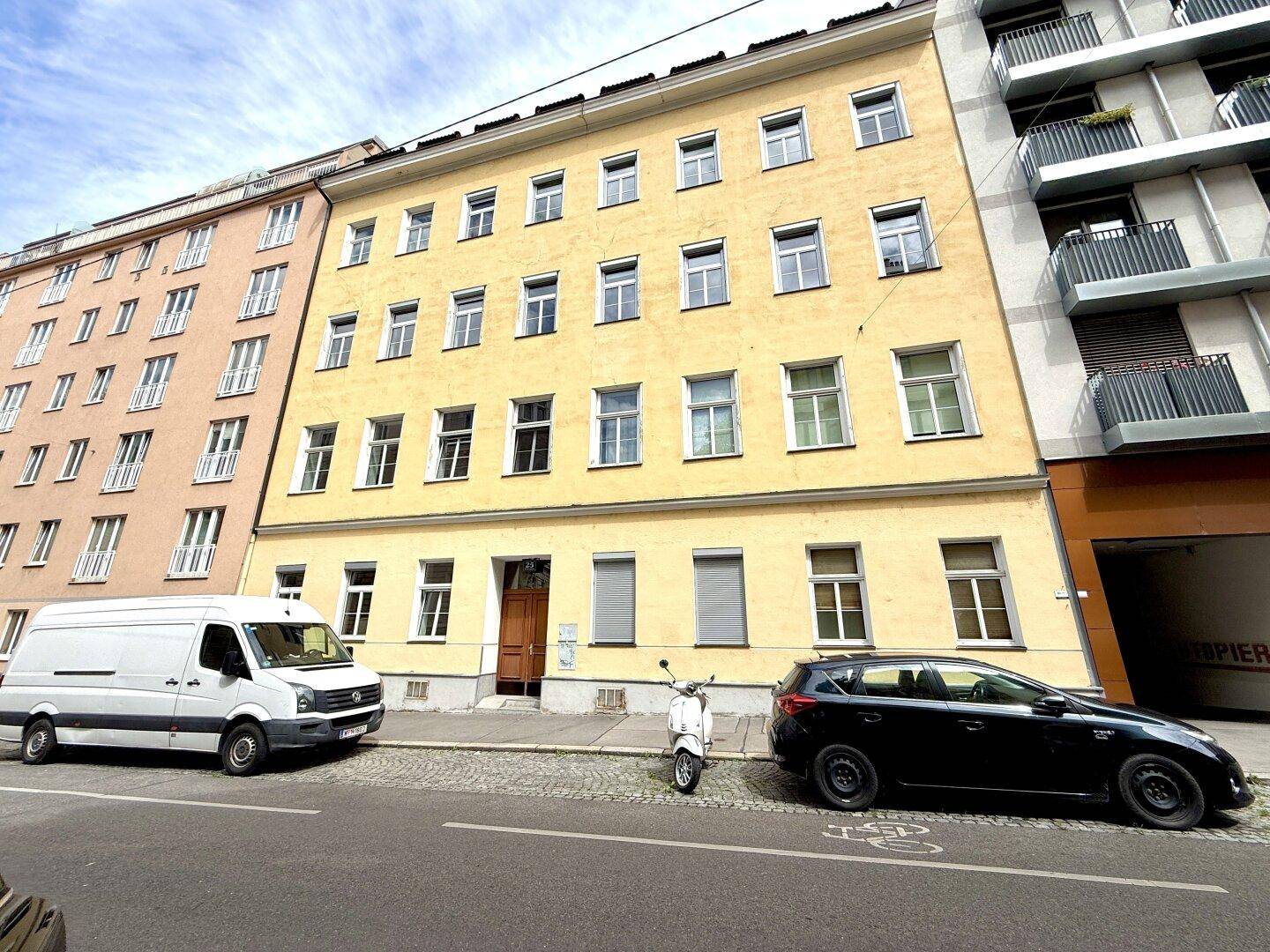Fassade eines traditionellen gelben Wohngebäudes mit vielen Fenstern und einem Roller davor.
