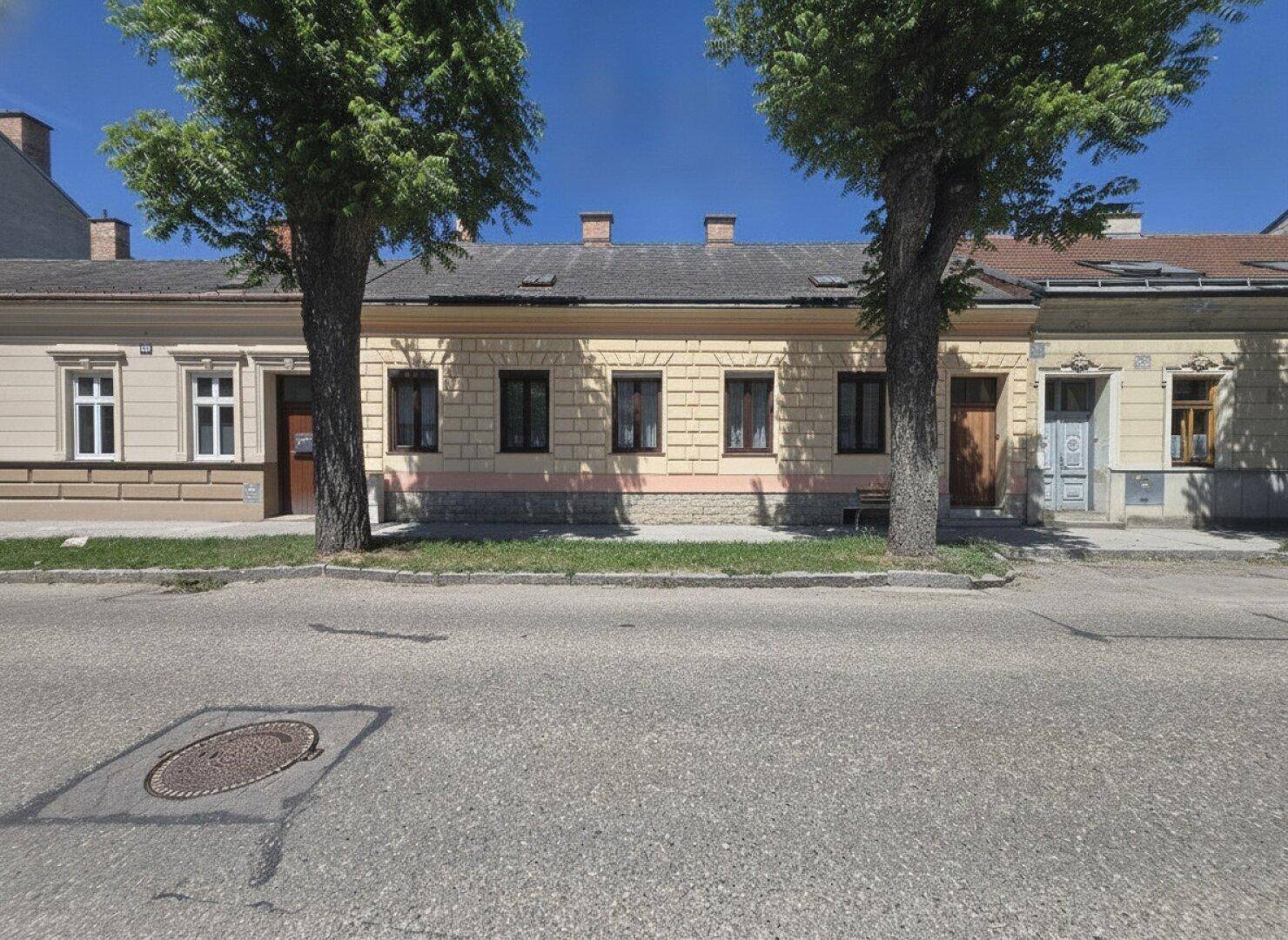 Ansicht der Gebäudefassade von der Straße aus mit zwei Bäumen davor.