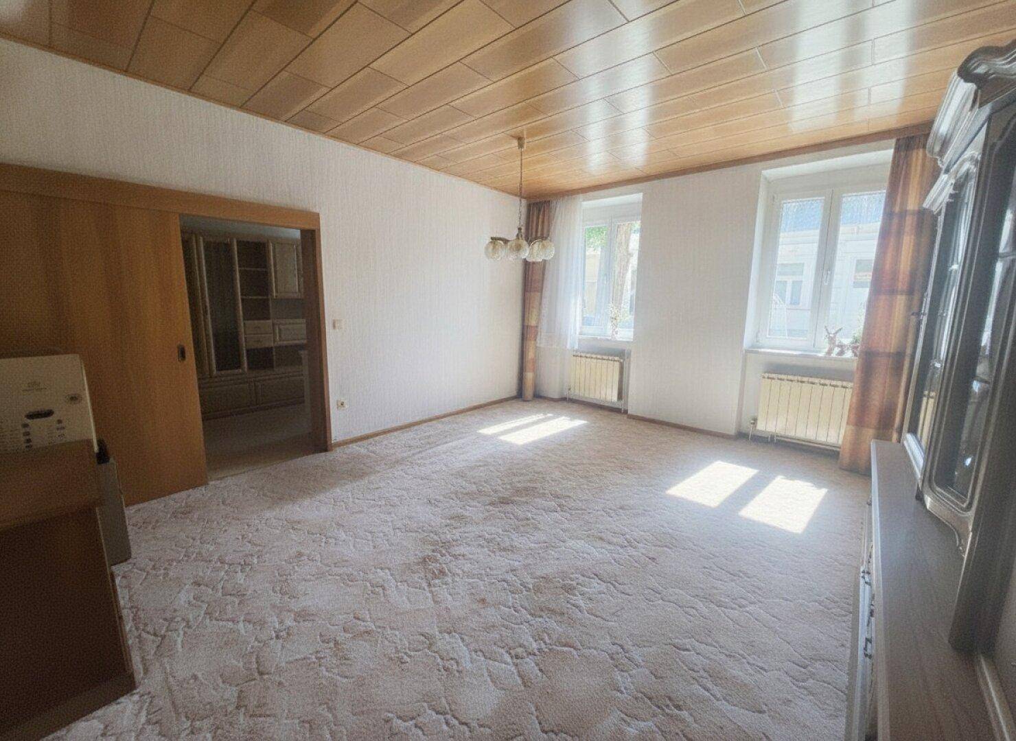 Geräumiges Wohnzimmer mit Teppichboden, Holzdecke und traditionellen Möbeln.