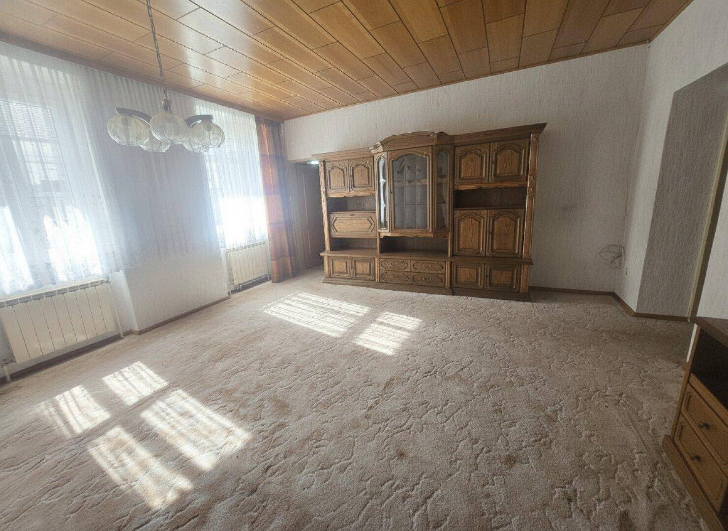 Helles Wohnzimmer mit großem Holzschrank, Teppichboden und Holzpaneeldecke.