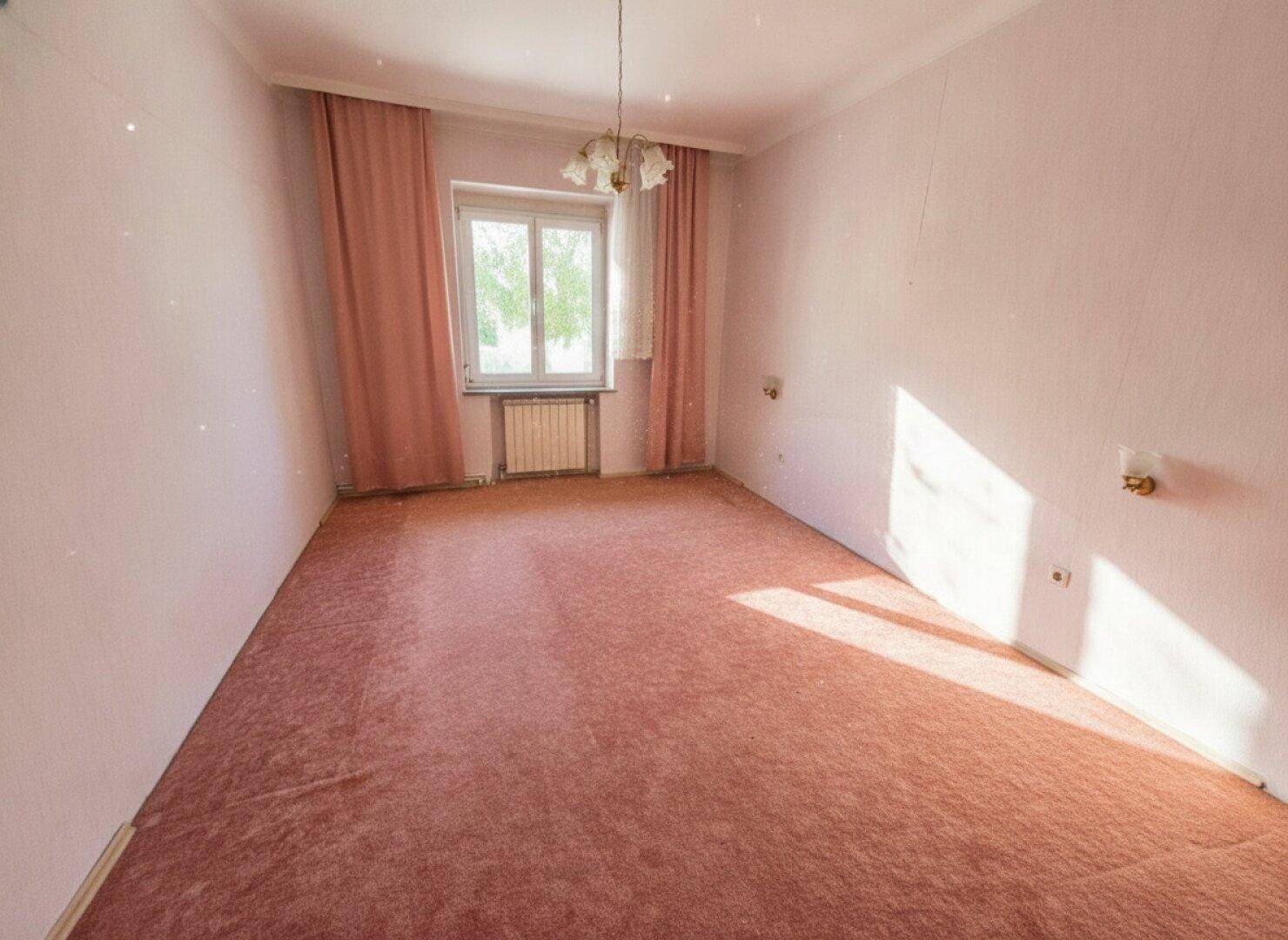 Leeres Schlafzimmer mit rosa Teppichboden und passenden Vorhängen am Fenster.