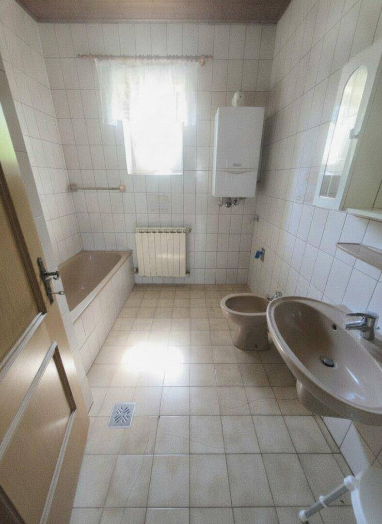 Badezimmer mit beigefarbenen Fliesen, Badewanne, Waschbecken und Fenster.