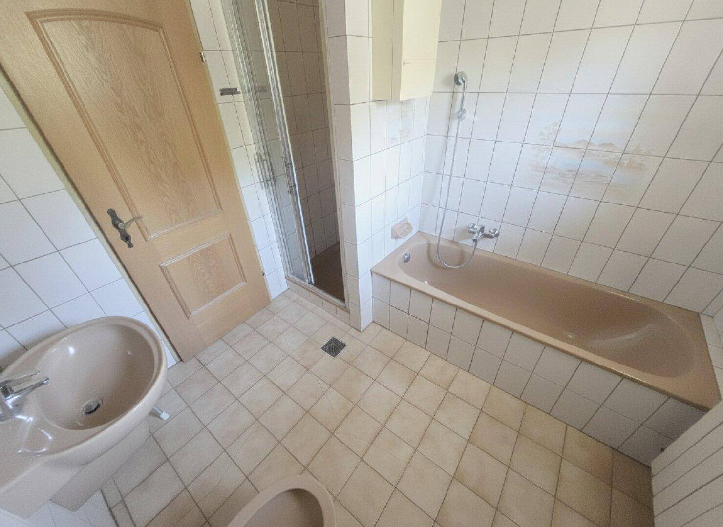 Badezimmer mit Badewanne, Duschkabine und Waschbecken in beigen Fliesen.