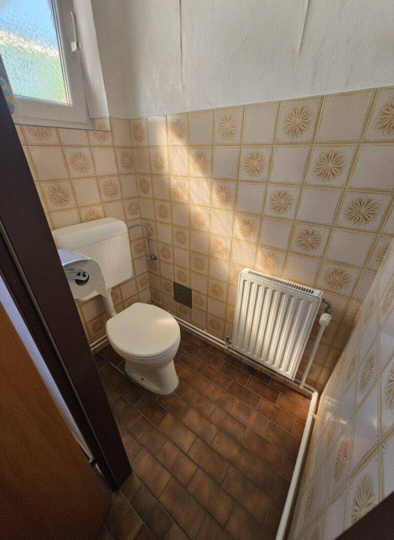 Separate Toilette mit gemusterten Fliesen, Fenster und Heizkörper.