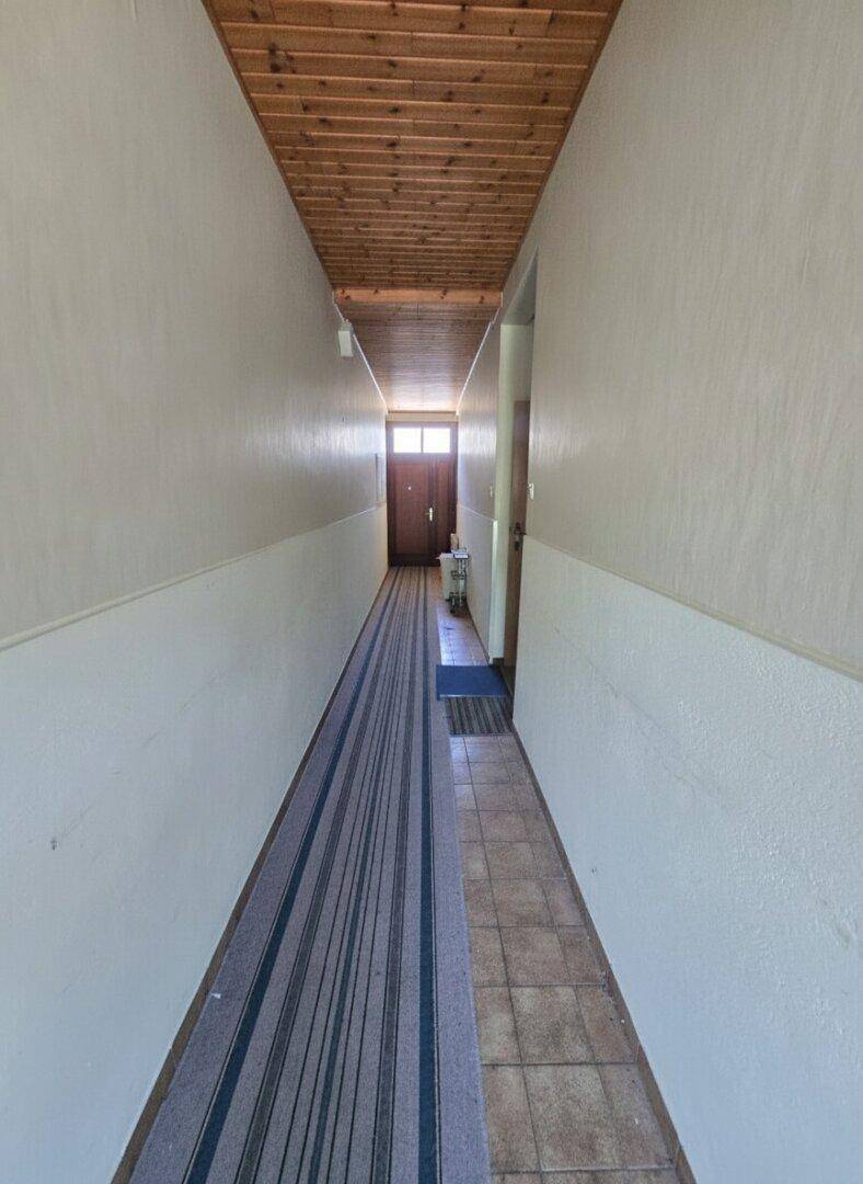 Langer Flur mit Holzpaneeldecke und Teppichläufer, der zum Eingang führt.