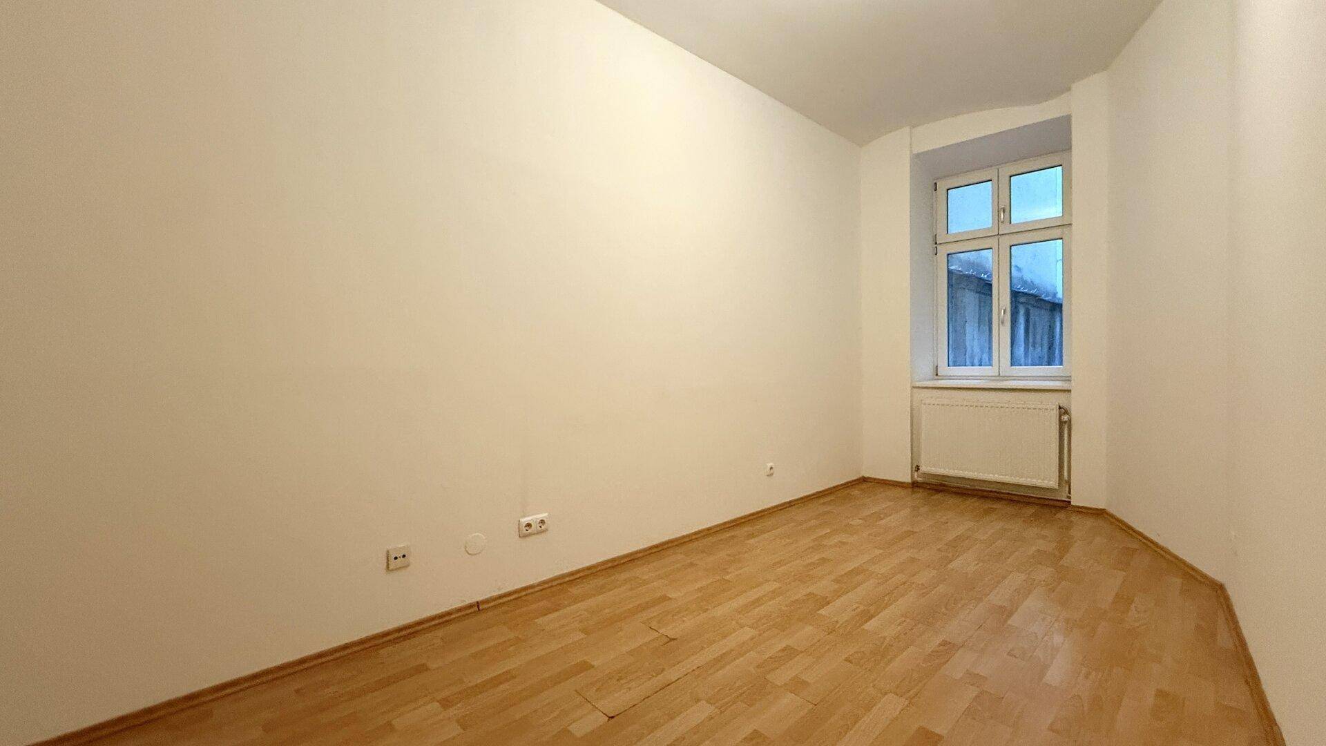 Helles Zimmer mit Laminatboden und einem Fenster, das viel Tageslicht hereinlässt.