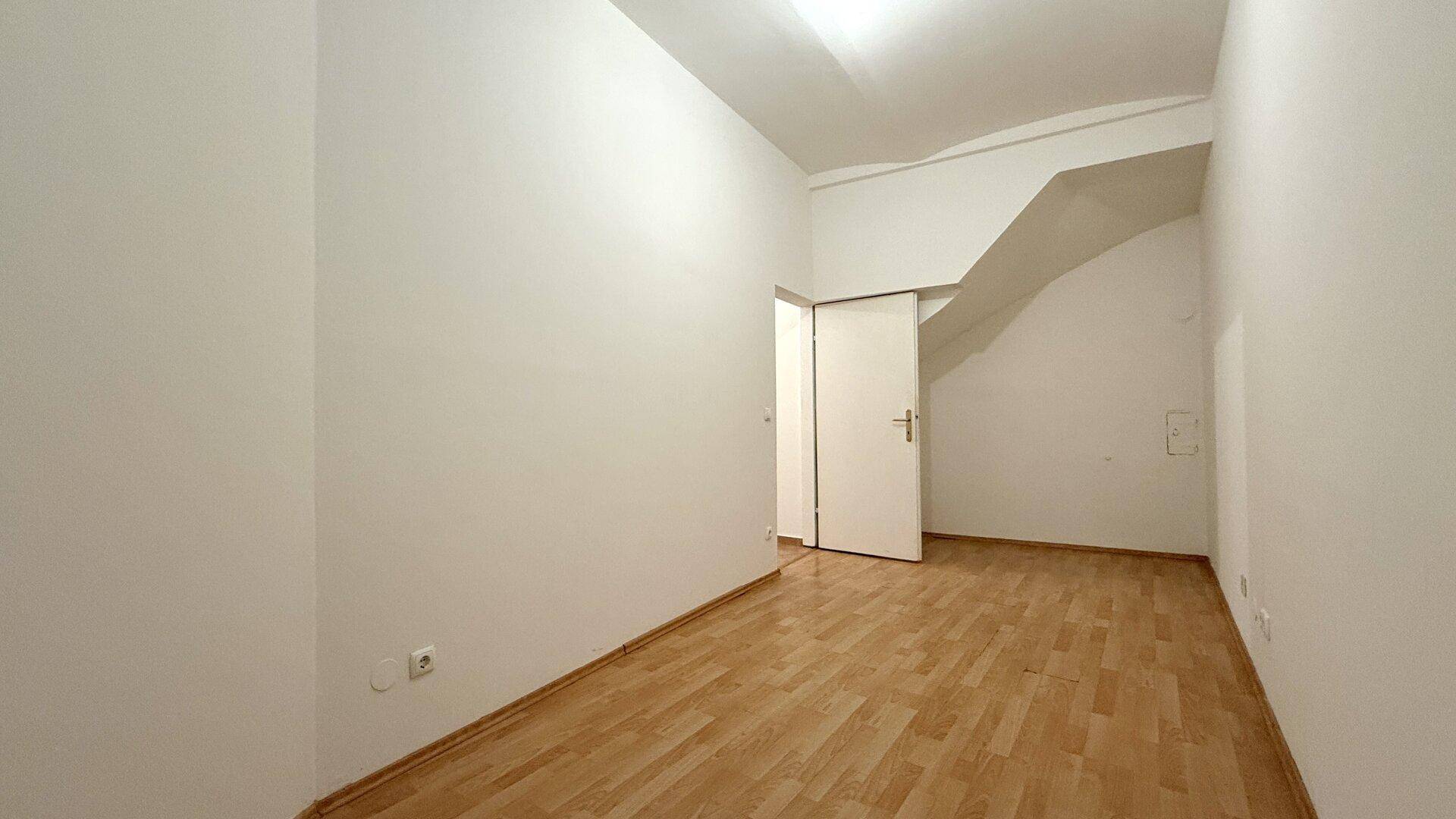 Leeres Zimmer mit Laminatboden und einer Tür, die zu einem weiteren Bereich führt.