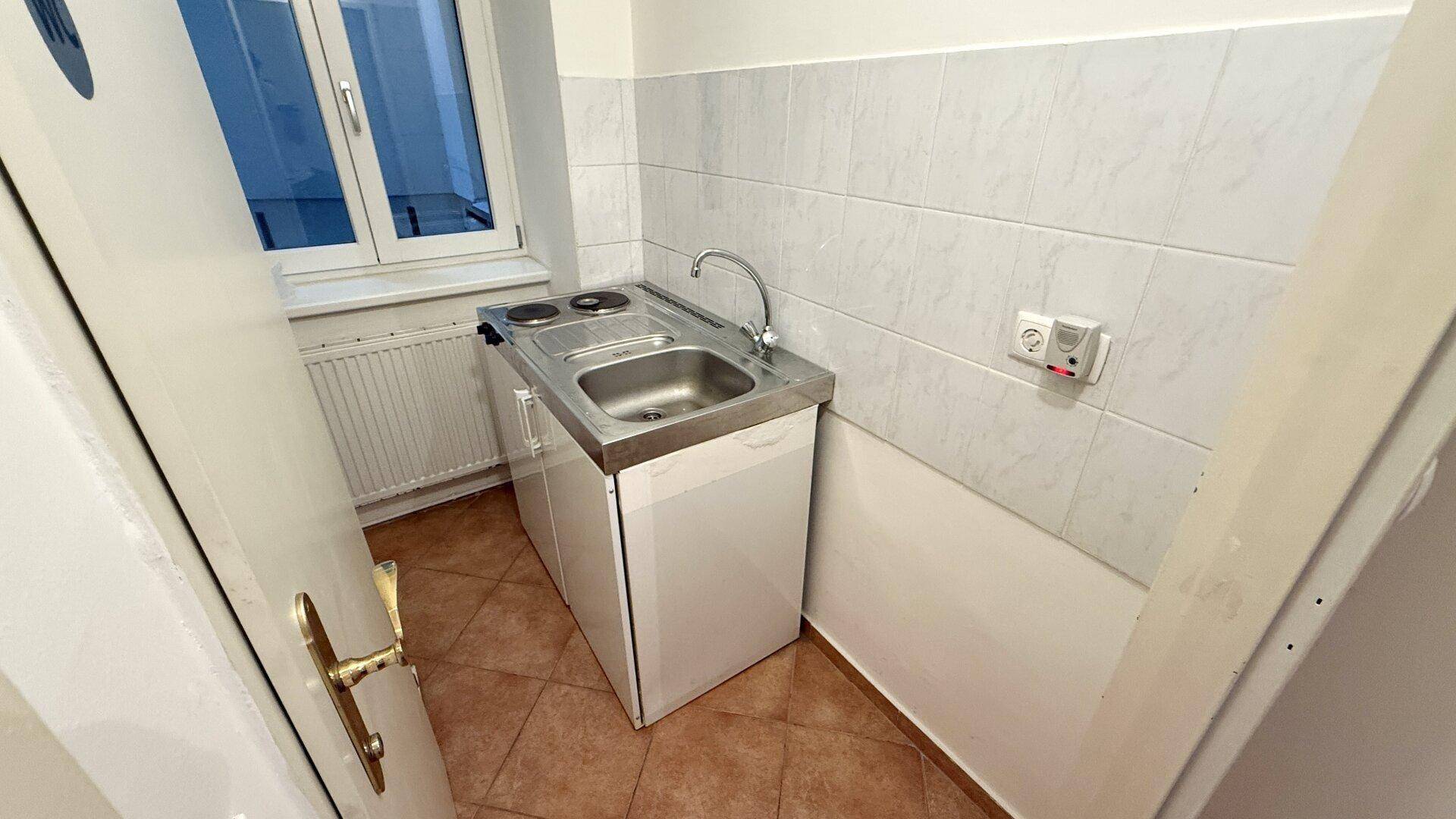 Kleine Kochnische mit Spüle, zwei Kochplatten und einem Fenster für Tageslicht.