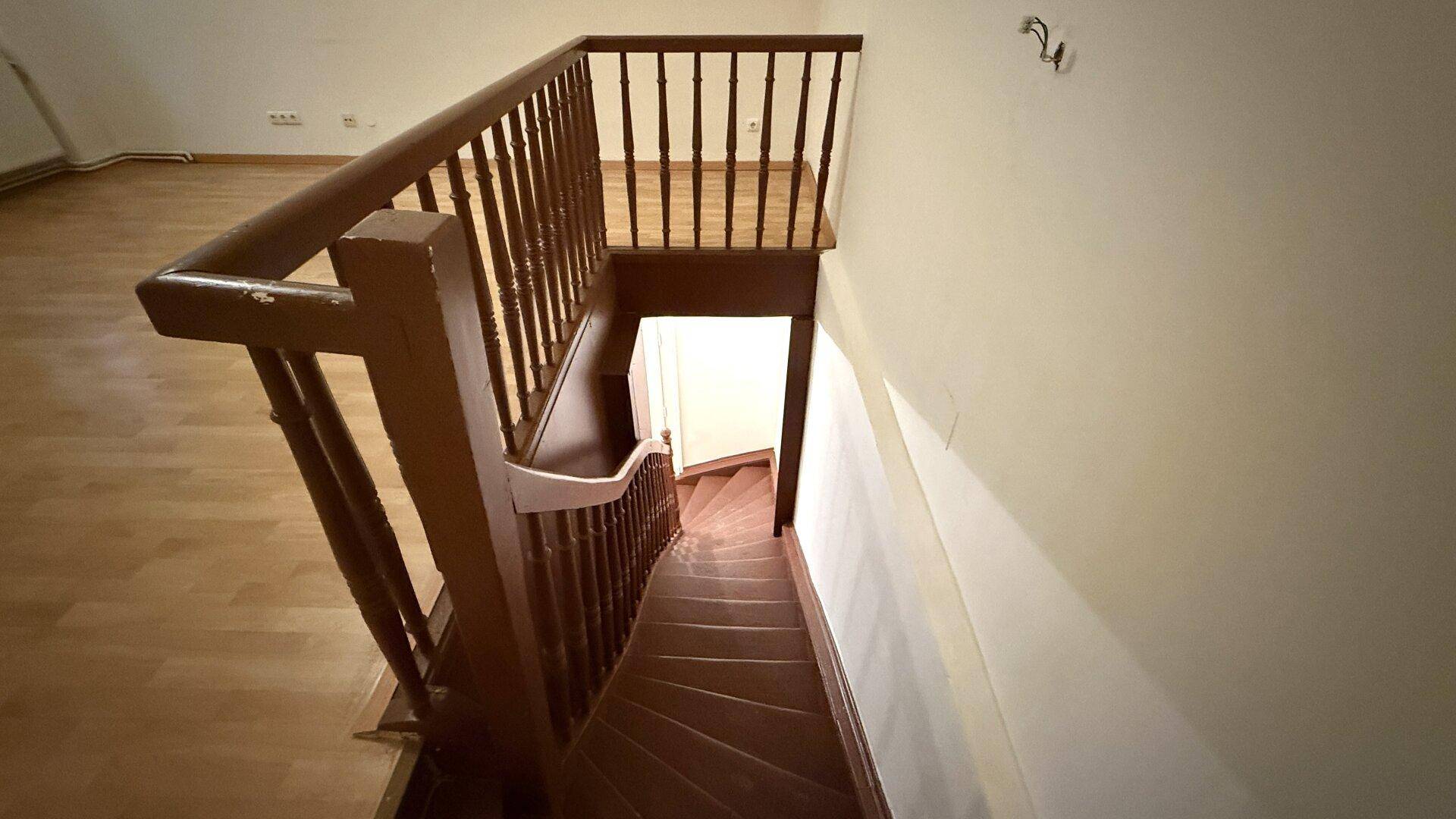 Holztreppe mit Geländer, die in eine untere Etage führt, mit hellem Laminatboden im oberen Bereich.