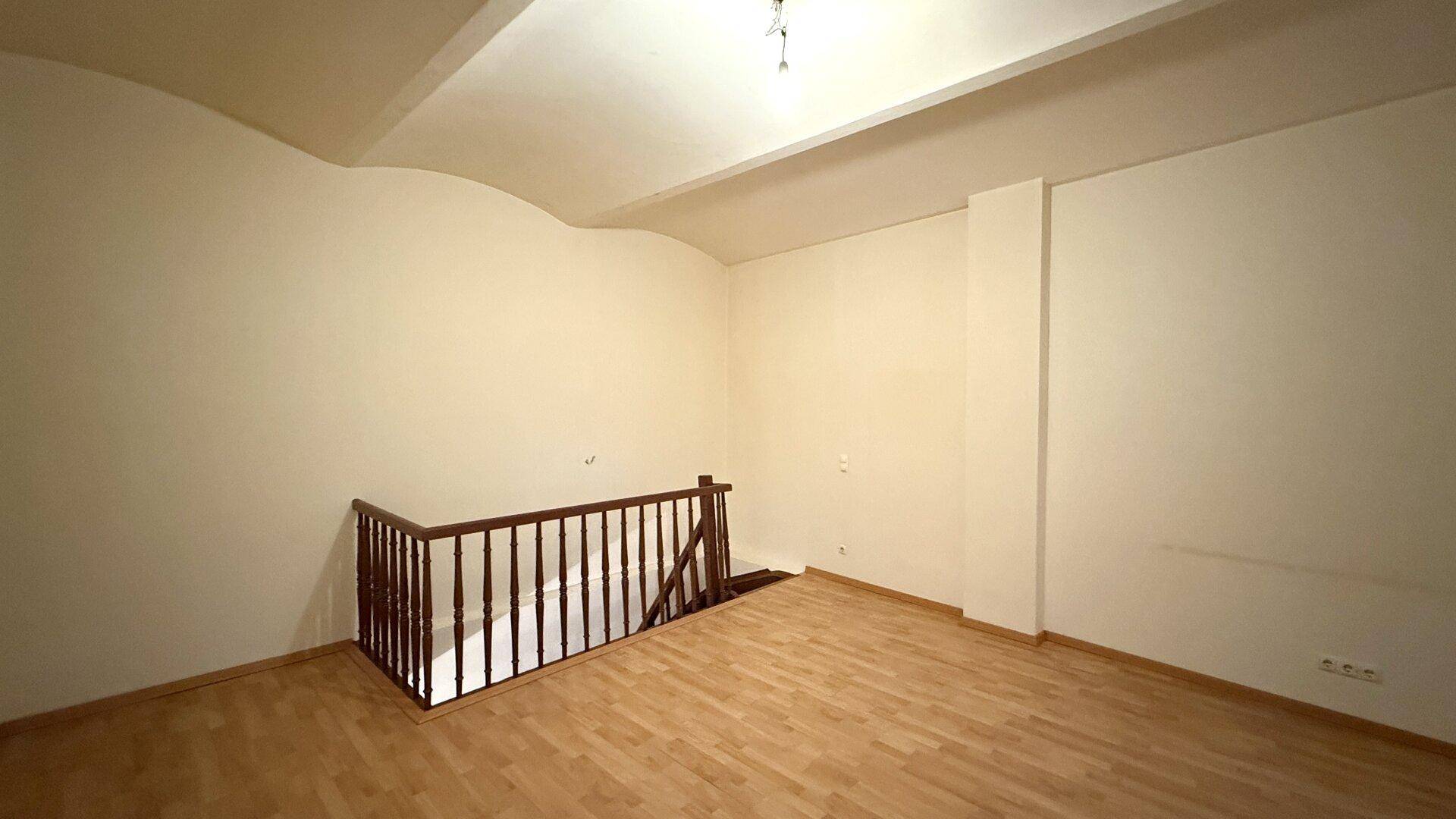 Heller, leerer Raum mit Laminatboden und einem Holzgeländer, das zu einer unteren Etage führt.