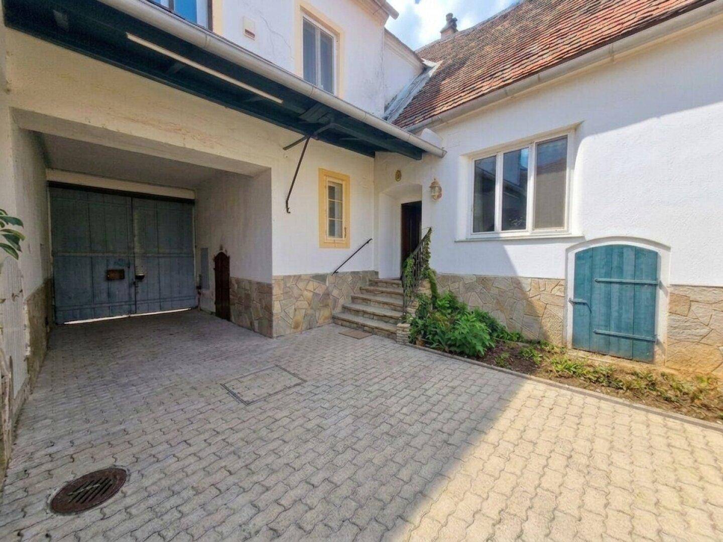 Eingangsbereich eines traditionellen Gebäudes mit gepflastertem Hof und großem Garagentor.