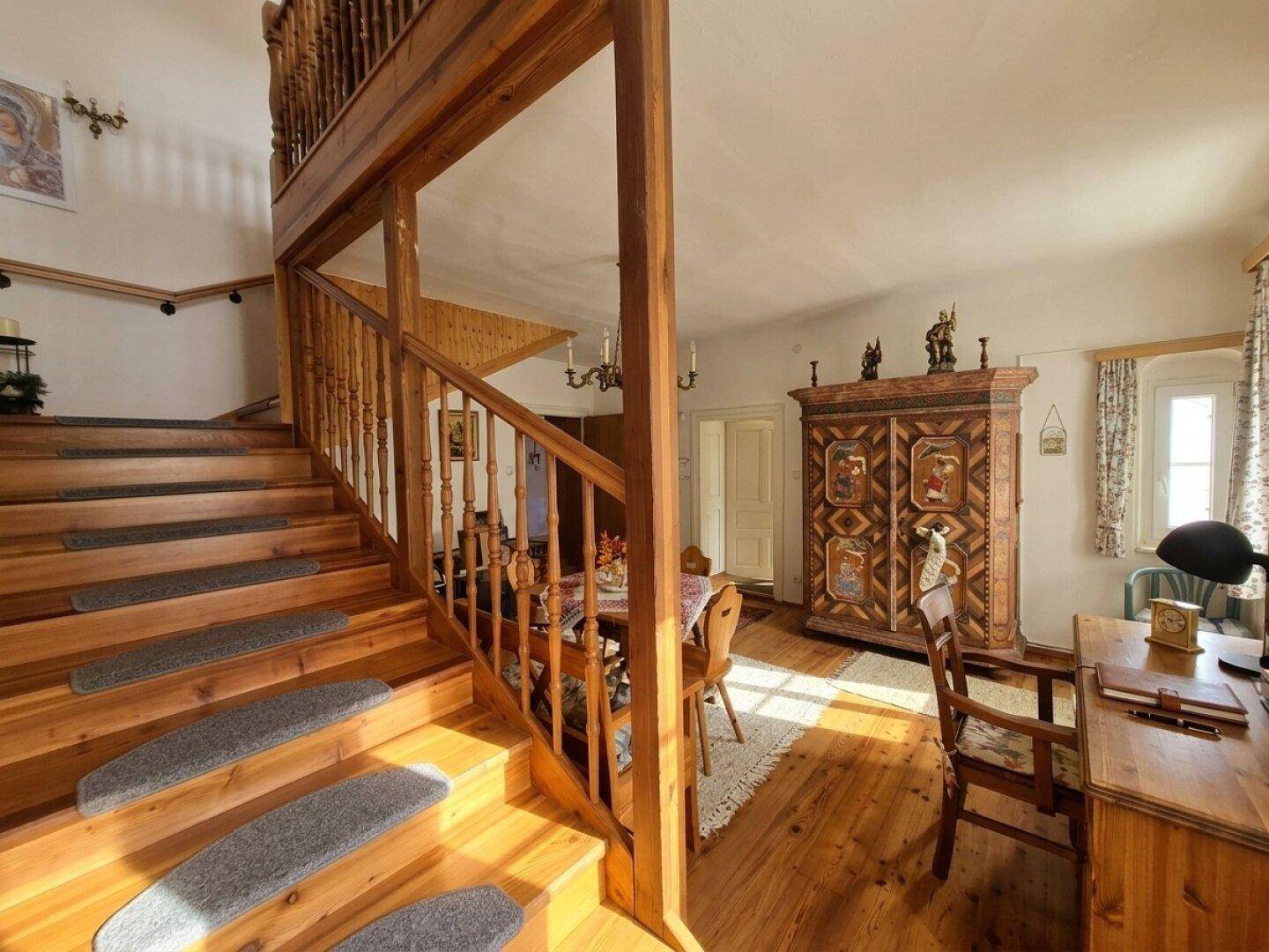 Rustikale Holztreppe in einem hellen Innenraum mit traditionellen Möbeln und Holzboden.