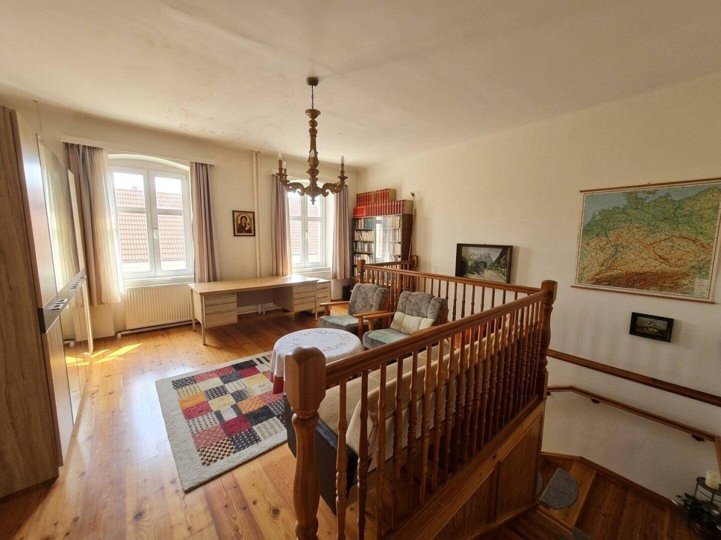 Heller Arbeitsbereich im Obergeschoss mit Holzboden, Schreibtisch und Blick nach draußen.