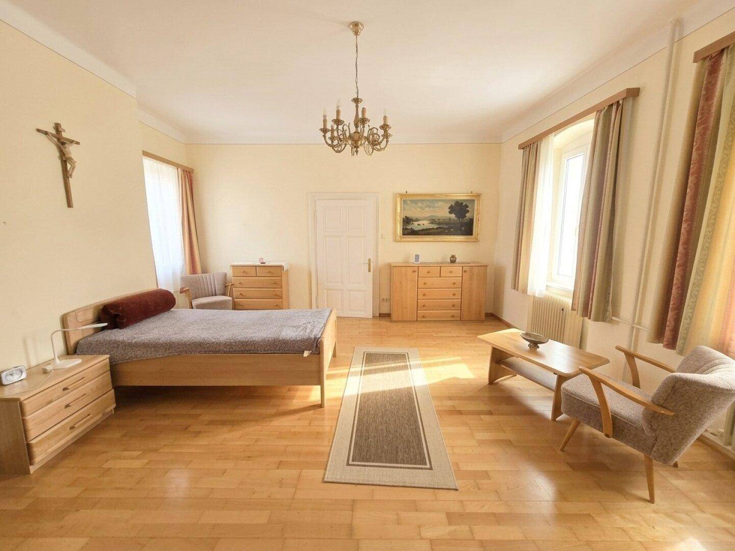 Helles Schlafzimmer mit Holzboden, schlichten Holzmöbeln und großen Fenstern.