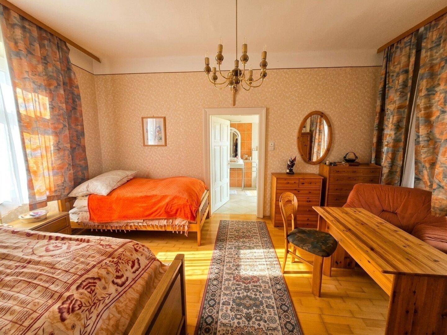 Gemütliches Schlafzimmer mit zwei Betten, Holzboden und Zugang zu einem weiteren Raum.