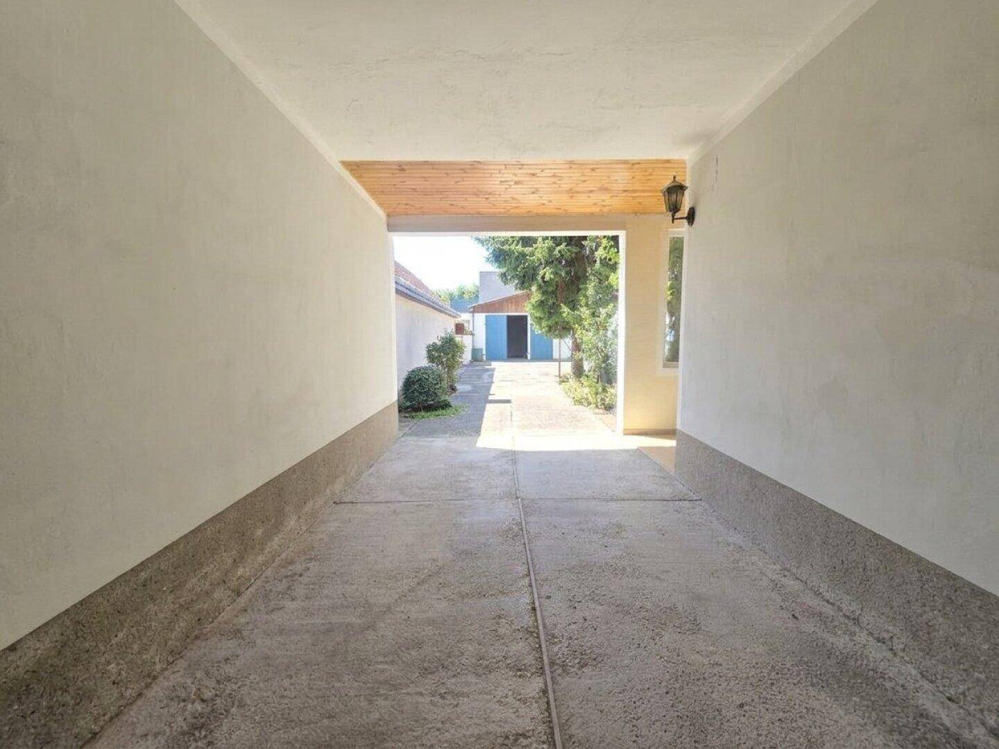Überdachte Zufahrt oder Carport mit Holzbalkendecke, die zum hinteren Bereich führt.
