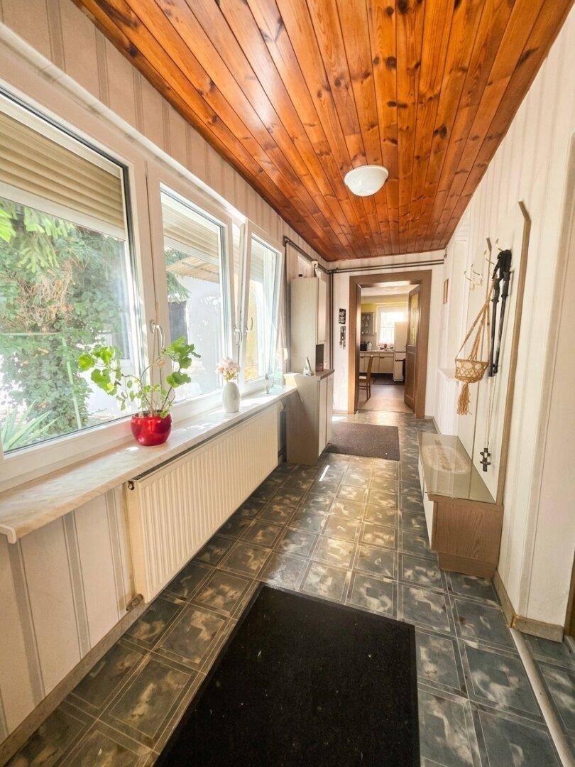 Heller Flur mit Holzpaneeldecke, Fliesenboden und großen Fenstern.