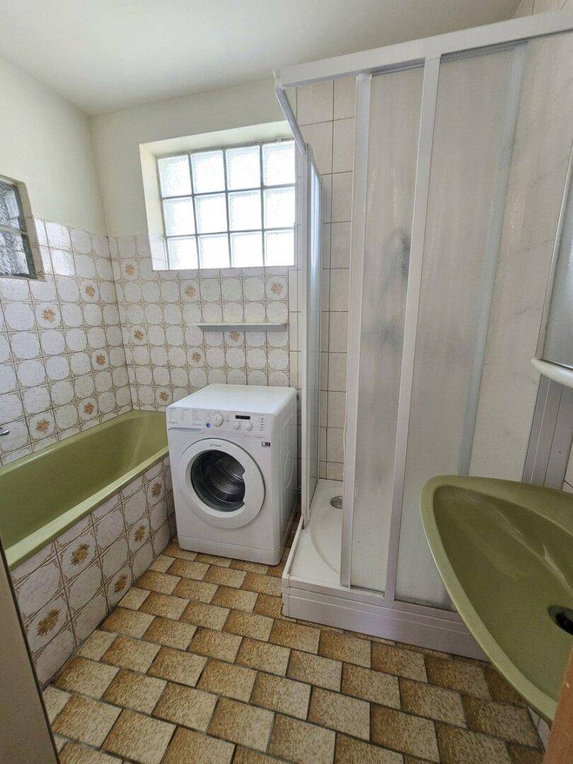 Badezimmer im Stil der 80er Jahre mit Badewanne, Dusche und Waschmaschine.