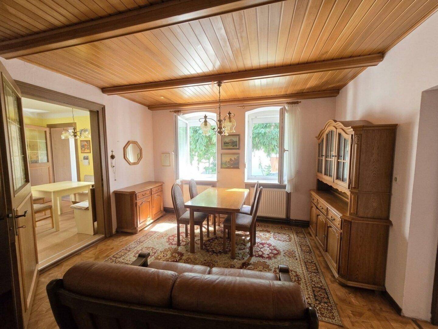 Gemütlicher Wohn- und Essbereich mit Holzbalkendecke, Teppich und traditionellen Möbeln.