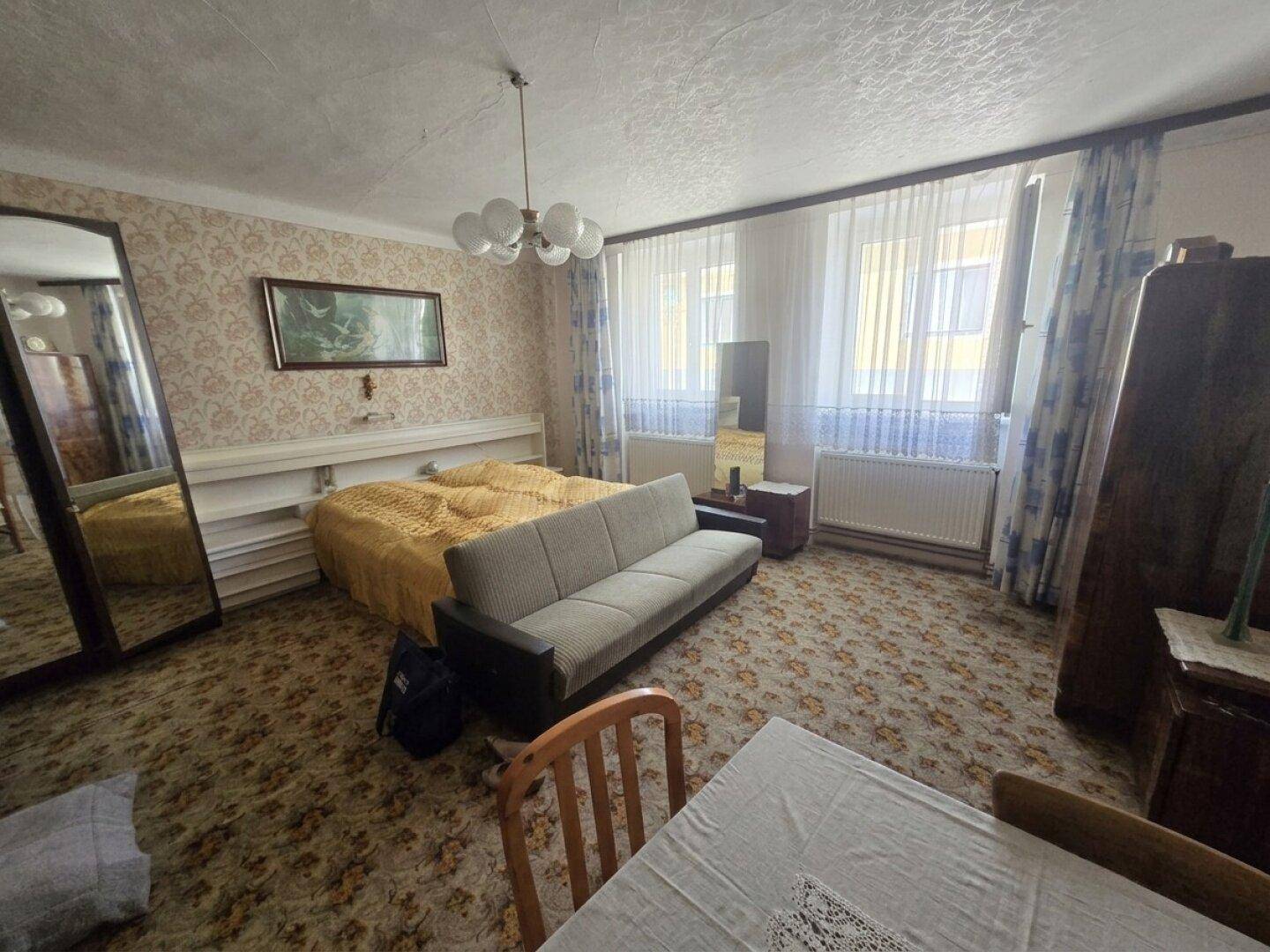 Schlafzimmer mit Teppichboden, Doppelbett, Sofa und großen Fenstern.