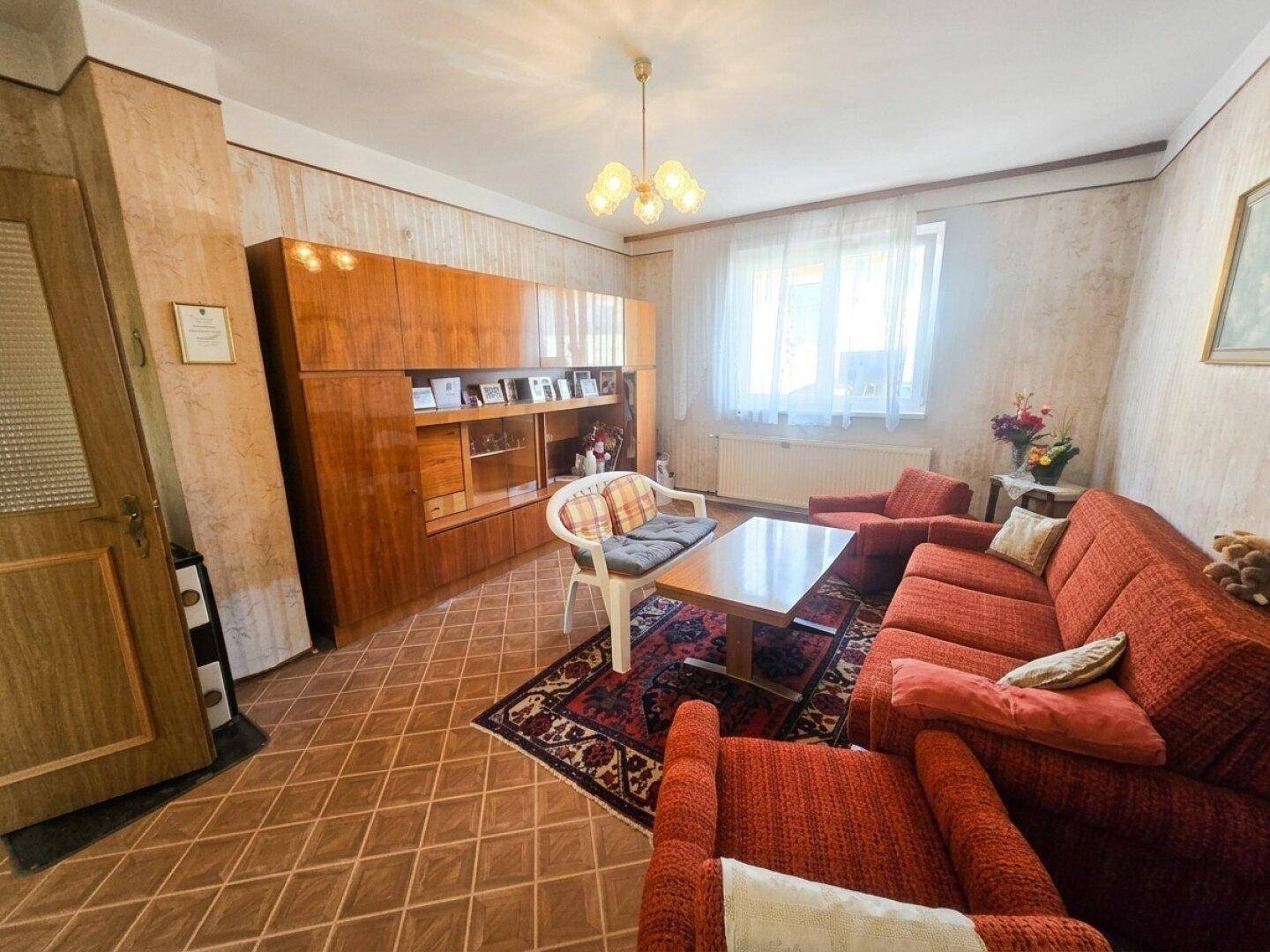 Wohnzimmer mit rotem Sofa, Holzschrankwand und gemustertem Fliesenboden.