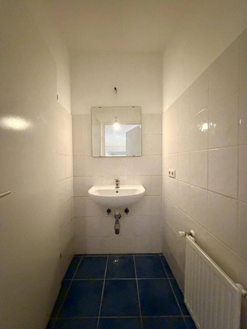Kleines Badezimmer mit weißen Wandfliesen, blauem Boden, Waschbecken und einem Spiegel.