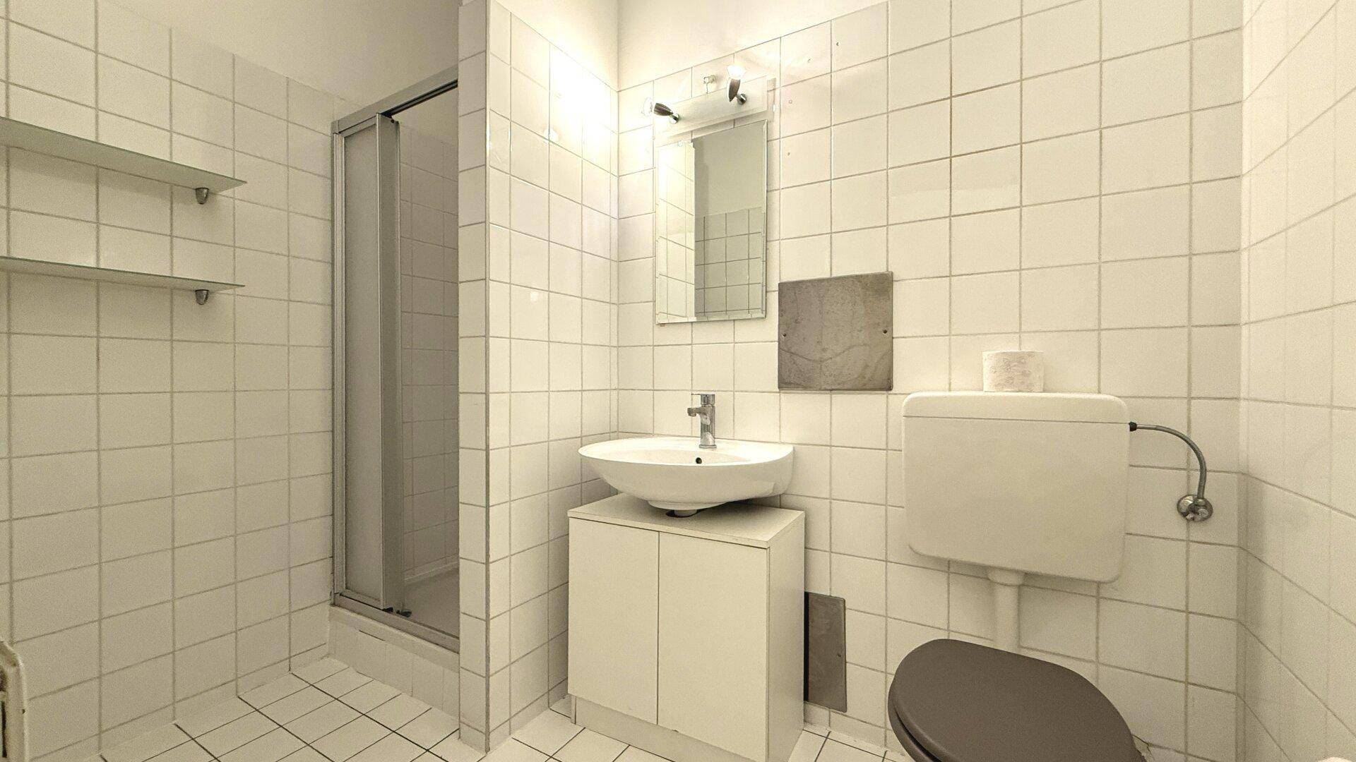 Gefliestes Badezimmer mit Dusche, Waschbecken und Toilette in schlichtem Design.
