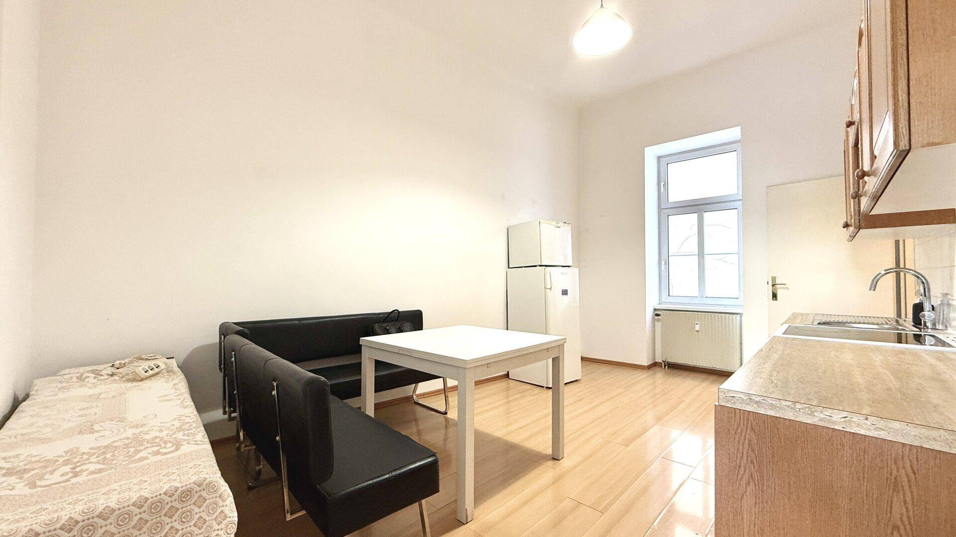 Küchenbereich mit Esstisch, Sitzbank und Kühlschrank, hell durch Fenster belichtet.