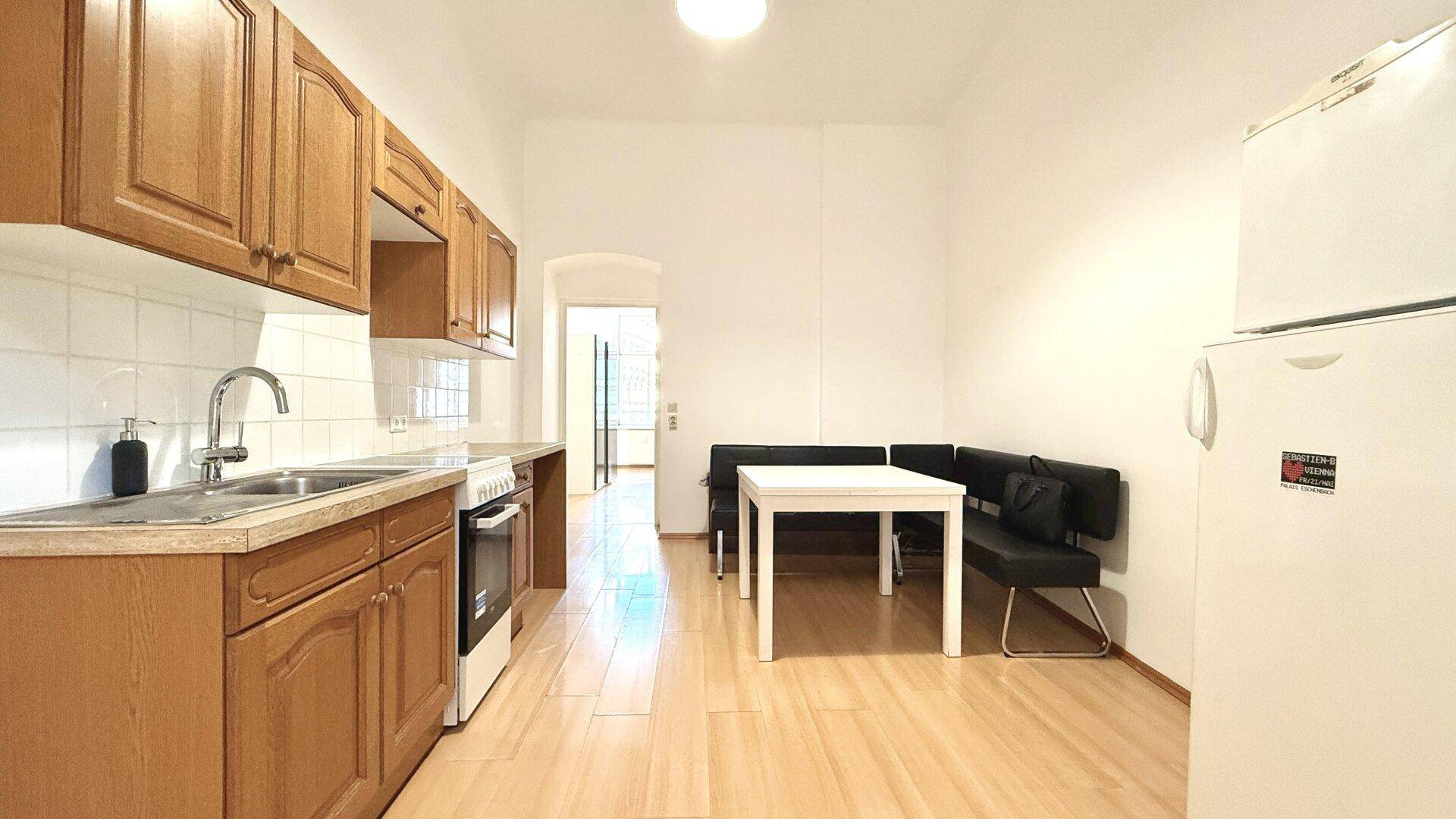 Längliche Küche mit Holzschränken, Essbereich und Kühlschrank, offen gestaltet.