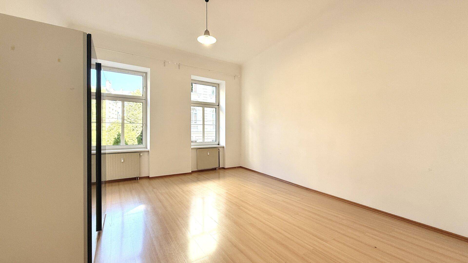 Geräumiges, helles Zimmer mit Laminatboden und hohen Decken, ideal für Wohn- oder Schlafbereich.