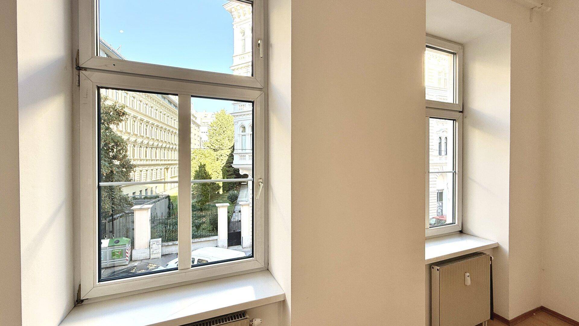 Blick aus dem Fenster eines hellen Zimmers auf die umliegenden Gebäude und Grünflächen.