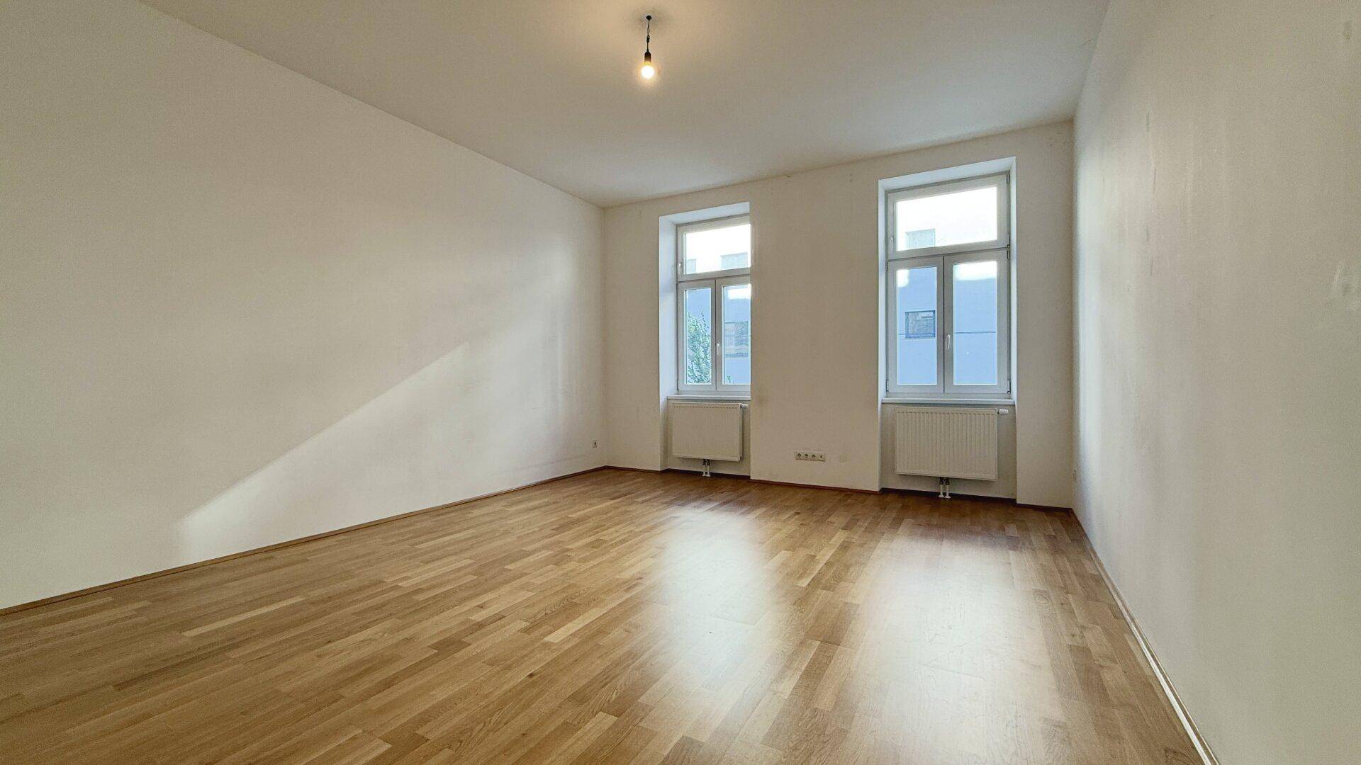 Geräumiges, helles Zimmer mit Holzboden und hohen Decken, bereit zur individuellen Gestaltung.