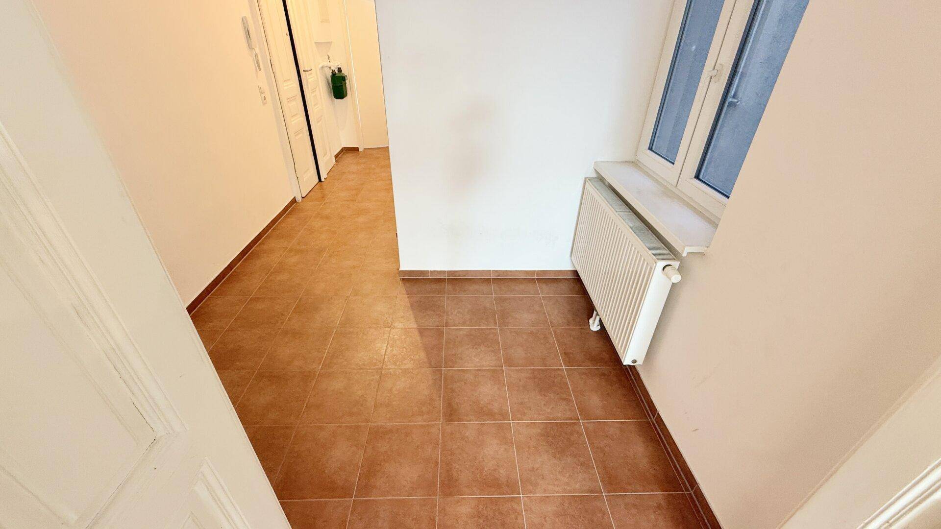 Heller Eingangsbereich mit Terracotta-Fliesenboden und Fenster, bietet Zugang zu weiteren Zimmern.