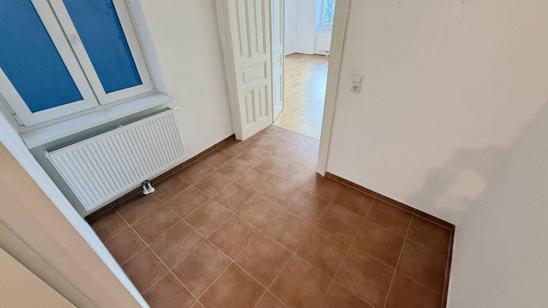 Geräumiger Flurbereich mit Terracotta-Fliesen und Blick in ein angrenzendes Zimmer mit Parkett.