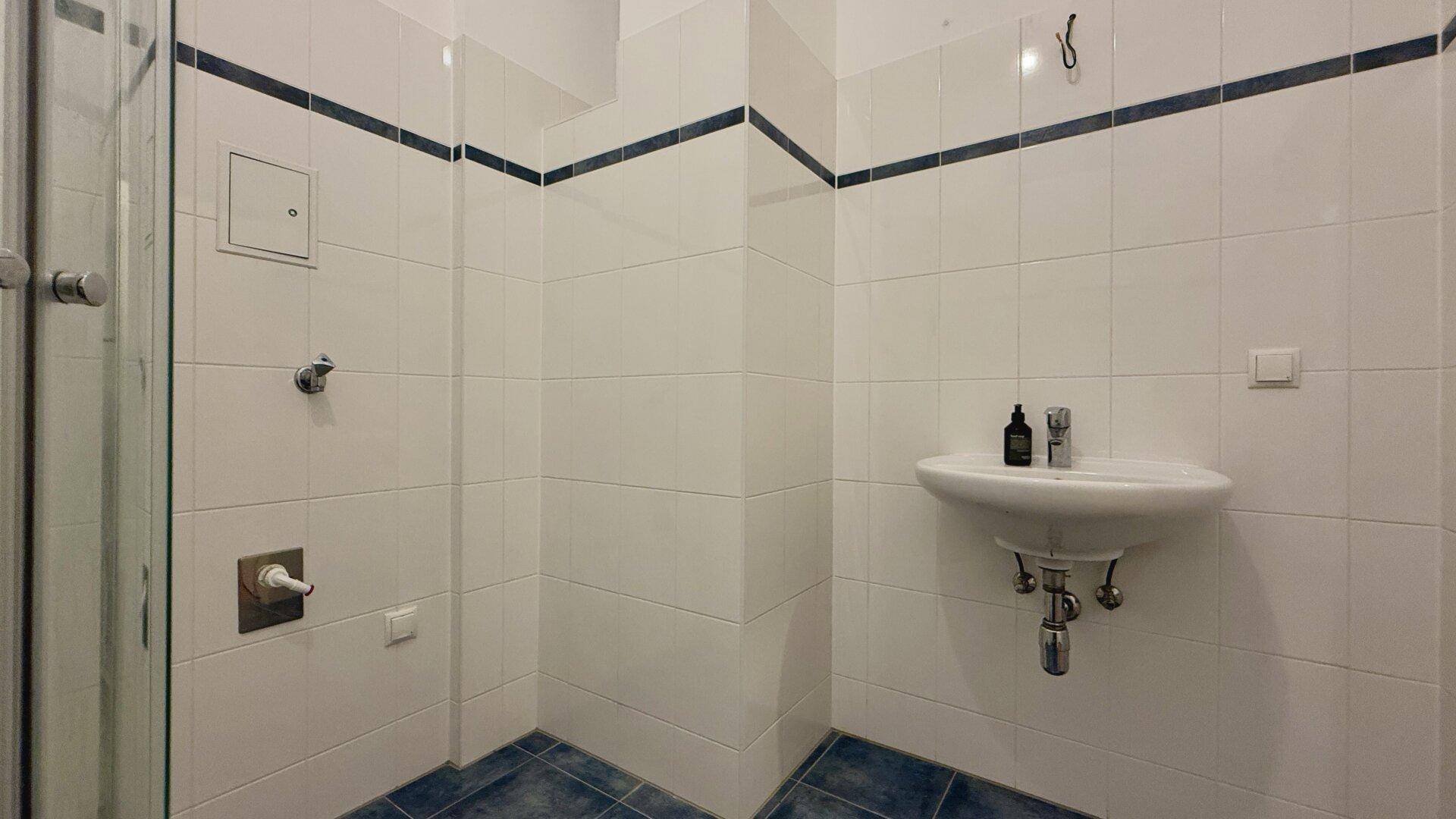 Badezimmer mit Waschbecken, weiß-blauen Fliesen und Duschbereich, sauber und funktional.