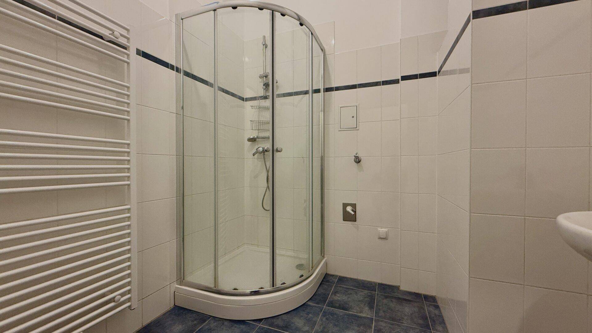 Badezimmer mit Duschkabine, beheiztem Handtuchhalter und weiß-blauen Fliesen, in gutem Zustand.
