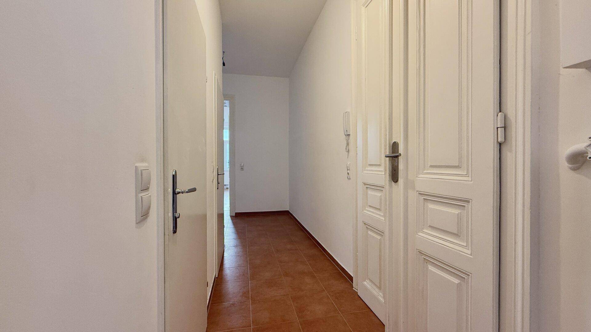 Langer, heller Flur mit Terracotta-Fliesenboden und mehreren Türen zu den angrenzenden Räumen.