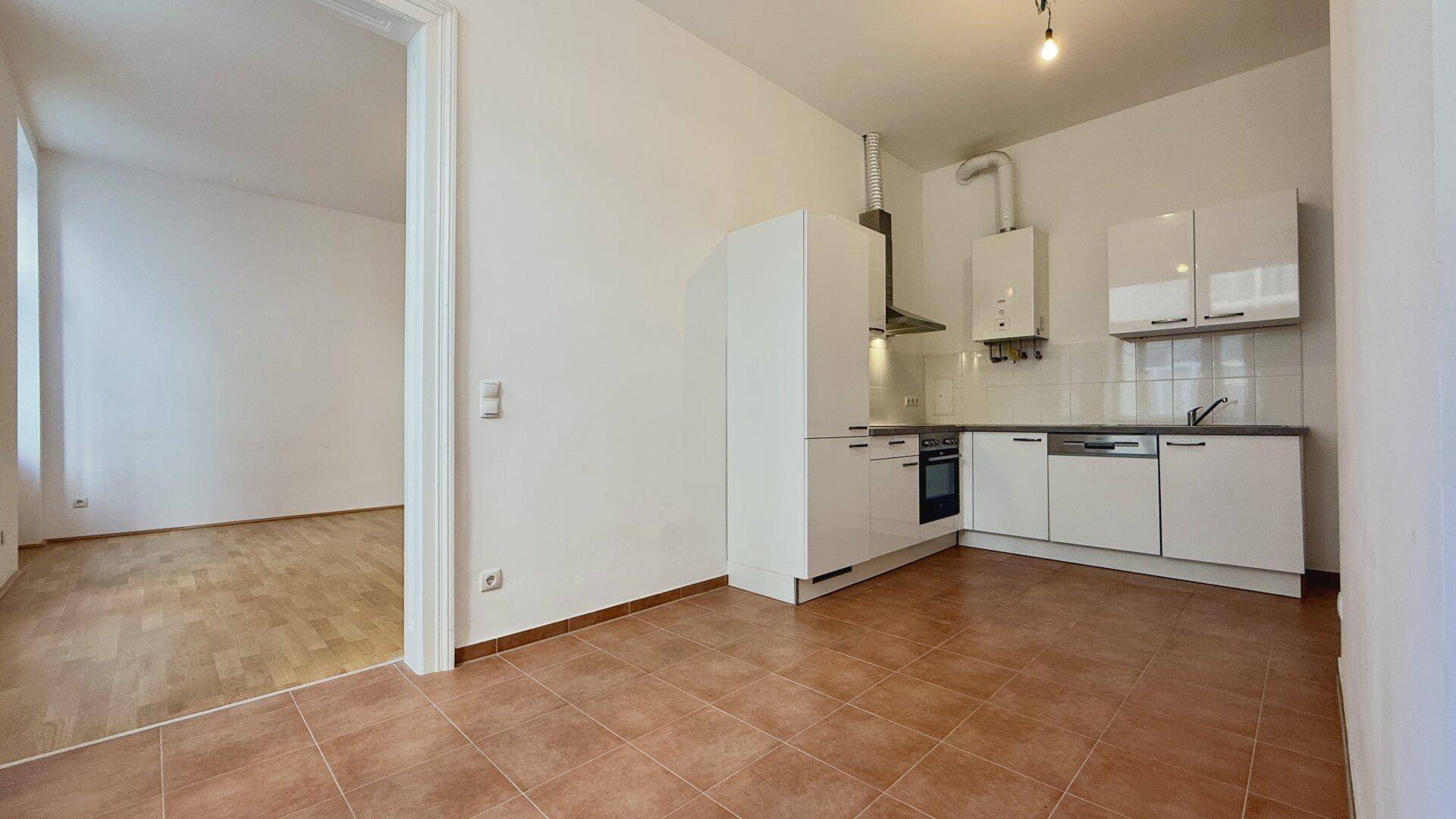 Offene Küche mit weißen Schränken und Terracotta-Fliesenboden, verbunden mit einem angrenzenden Zimmer.