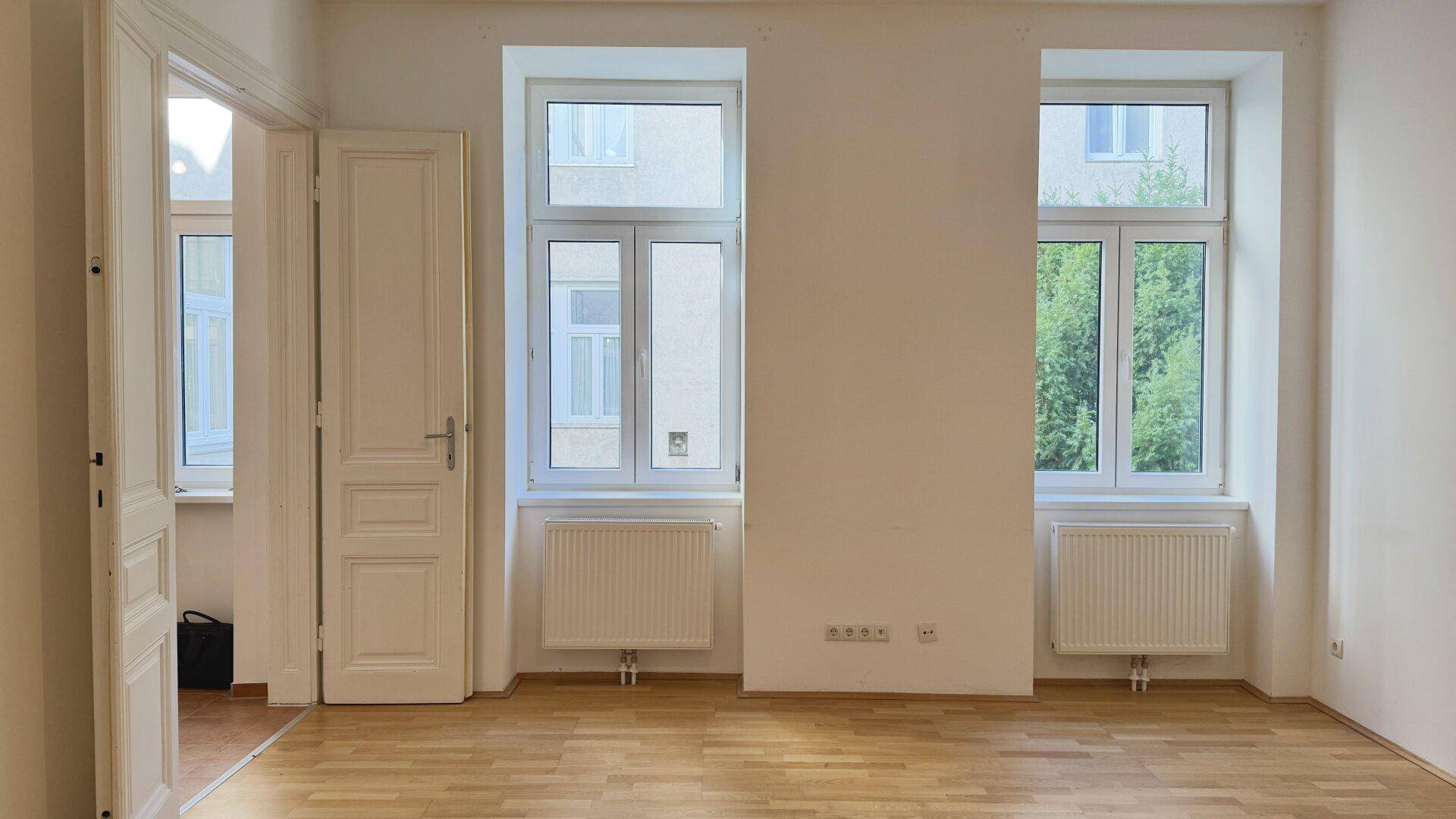 Großes, helles Zimmer mit Parkettboden und zwei Fenstern, ideal für Wohn- oder Schlafzwecke.