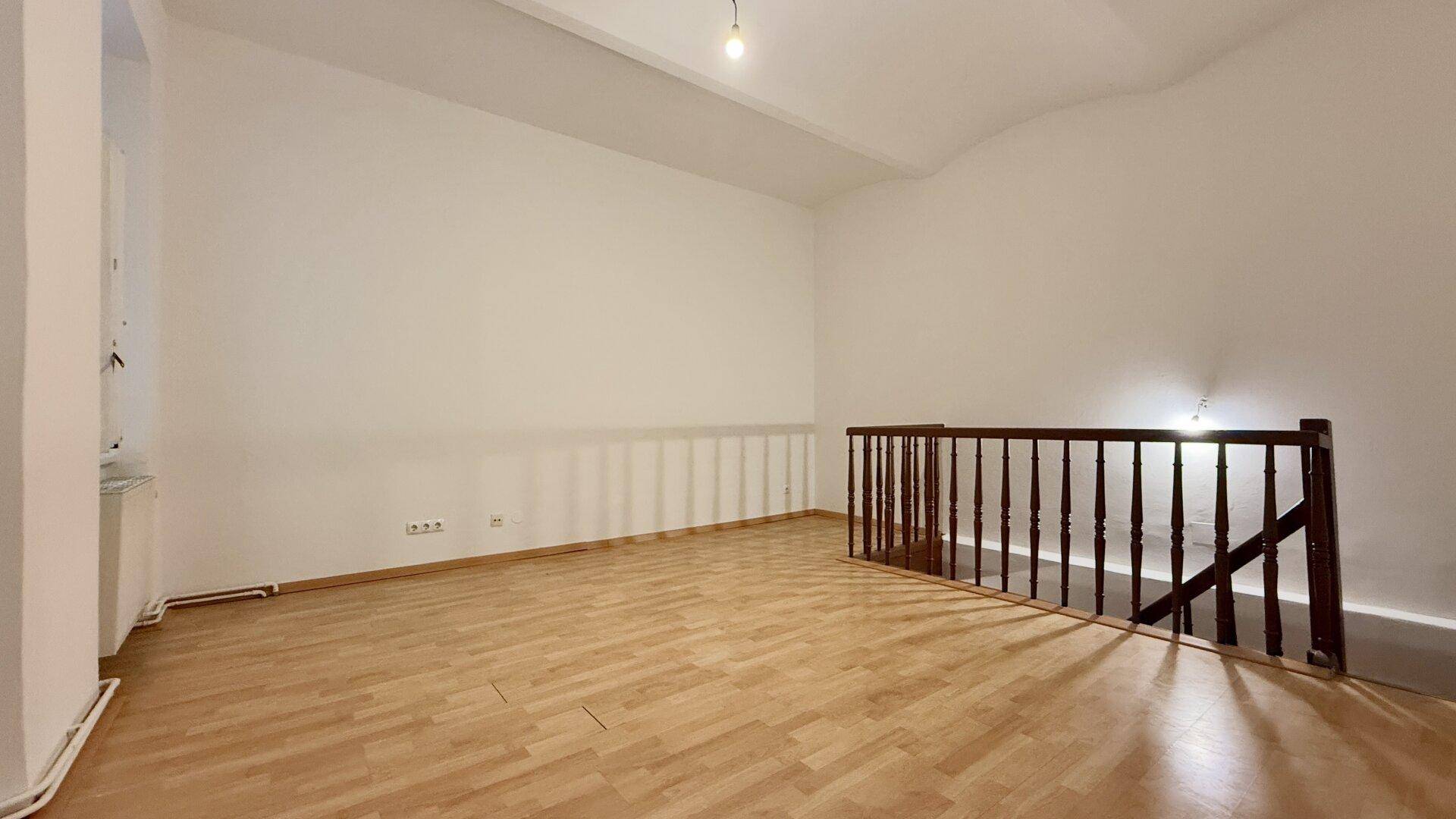 Heller, leerer Raum mit Holzboden und einer Holztreppe, die in eine andere Etage führt.