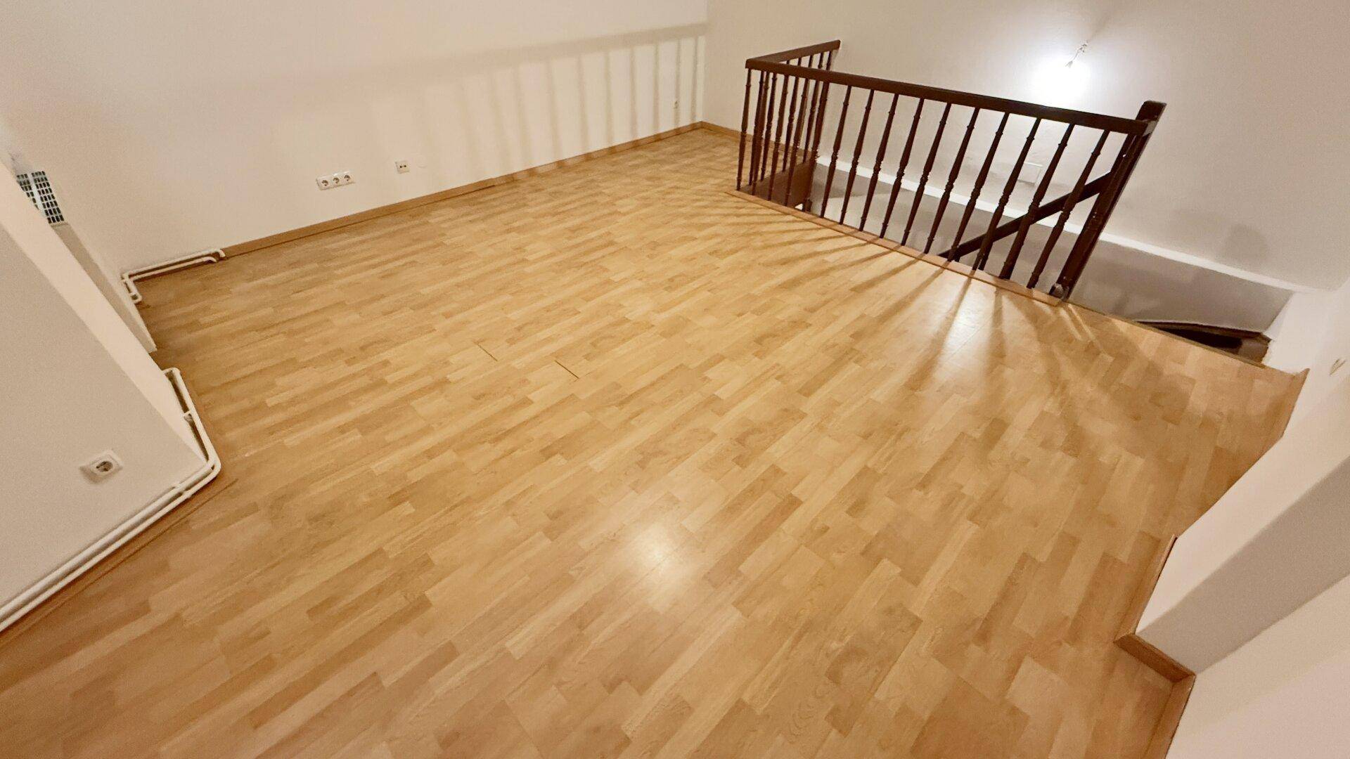 Blick von oben auf den Holzboden und das Holztreppengeländer in einem hellen Raum.