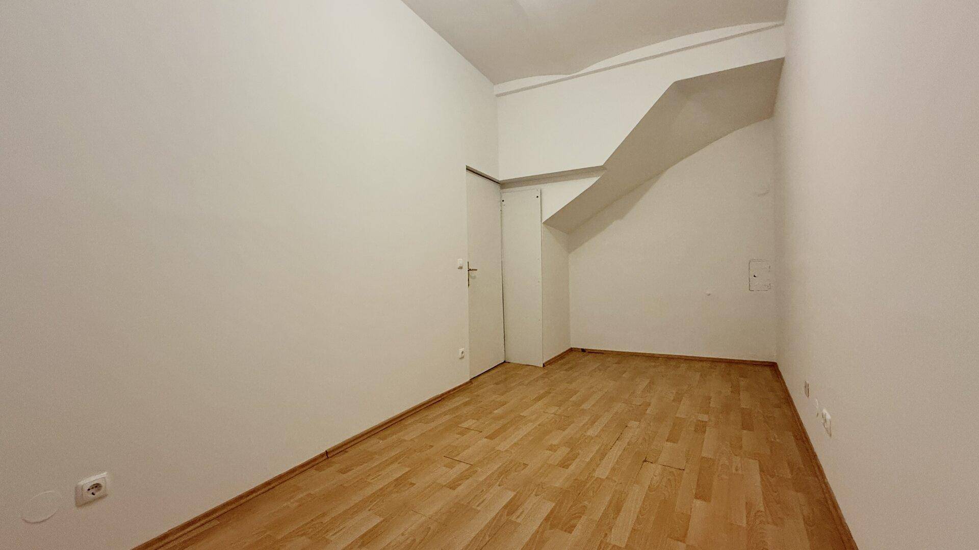 Leerer Raum mit Holzboden, weißen Wänden und einer interessanten Deckenkonstruktion.