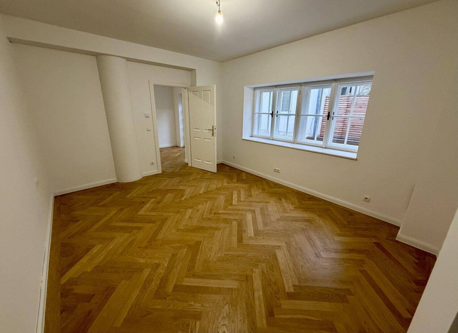 Großzügiges Wohnzimmer mit neu verlegtem Fischgrätparkett und Blick nach draußen.