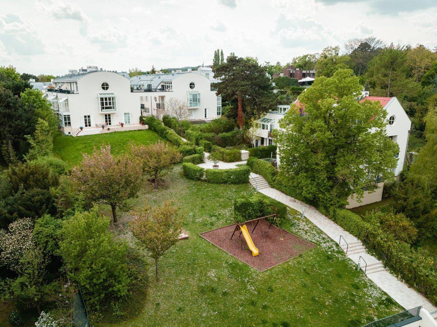 Weitläufige Gartenanlage mit Spielplatz und mehreren Wohngebäuden im Hintergrund.